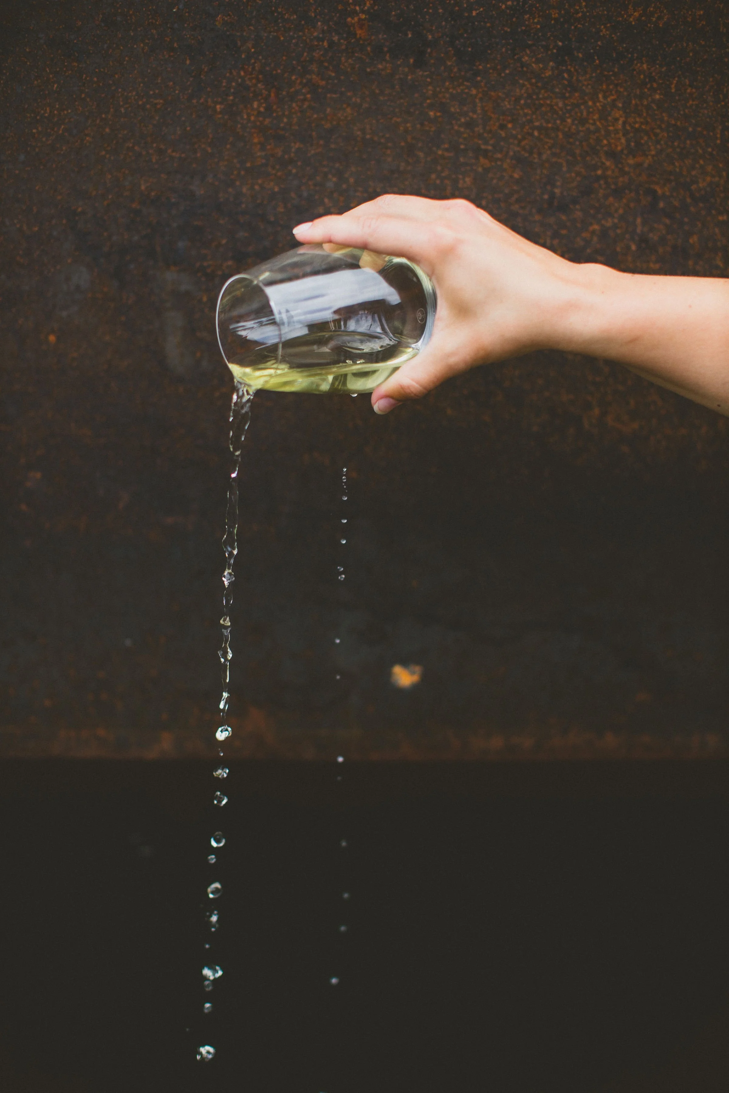 A person's hand holding a glass of wine tilted in Dundee, Oregon, with wine spilling out as drops fall downward during a branding photoshoot.
