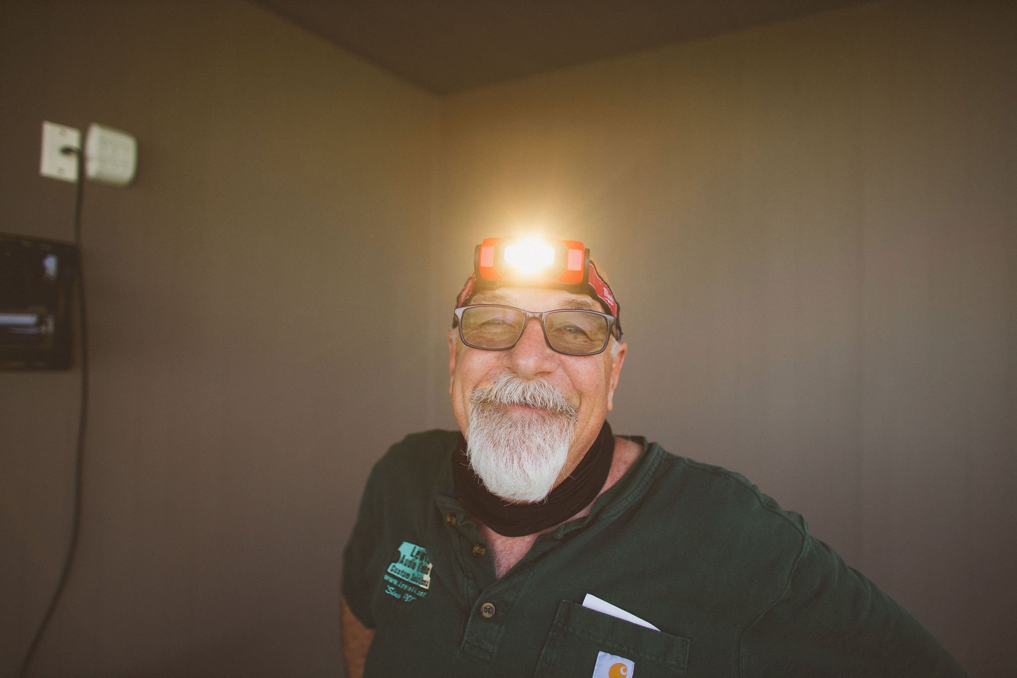 A man with glasses and a white beard, wearing a headlamp and a black shirt, smiling indoors during a branding photoshoot in Newberg, Oregon.