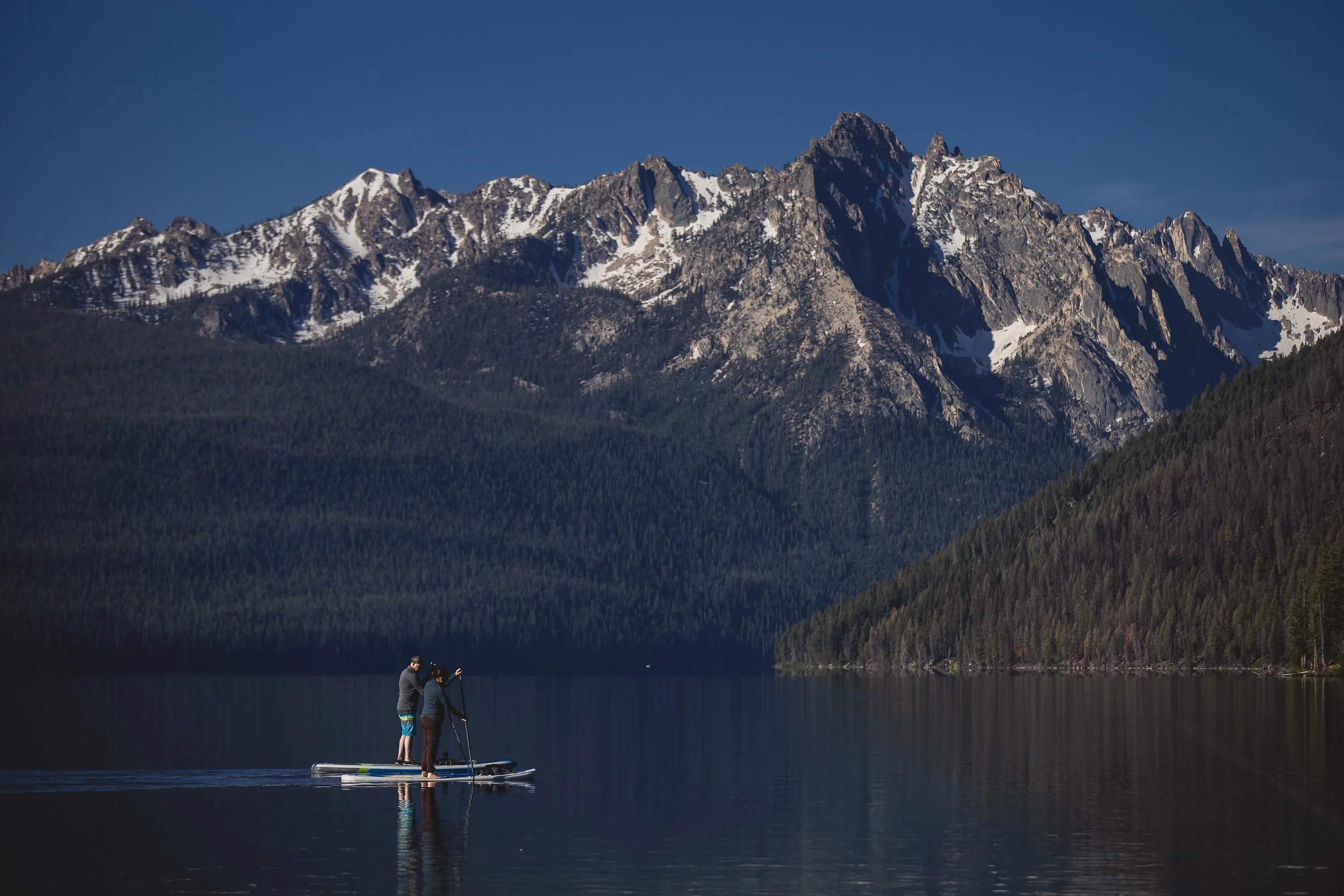 A couple paddle boarding on Red Fish Lake at the base of the Sawtooth Mountains during a branding photoshoot in Stanley Idaho.