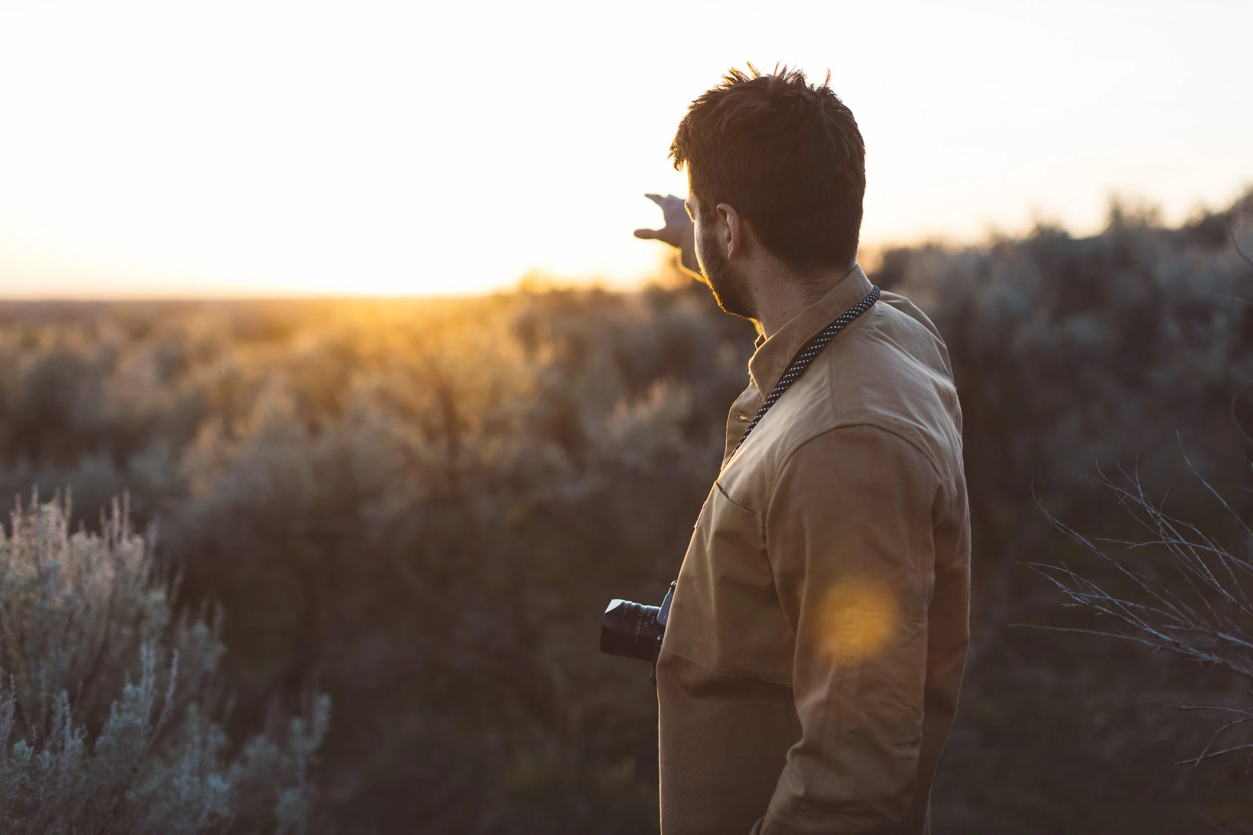 Young creative entrepreneur pointing into the distance with a camera around his neck during a branding photoshoot in the Boise Foothills