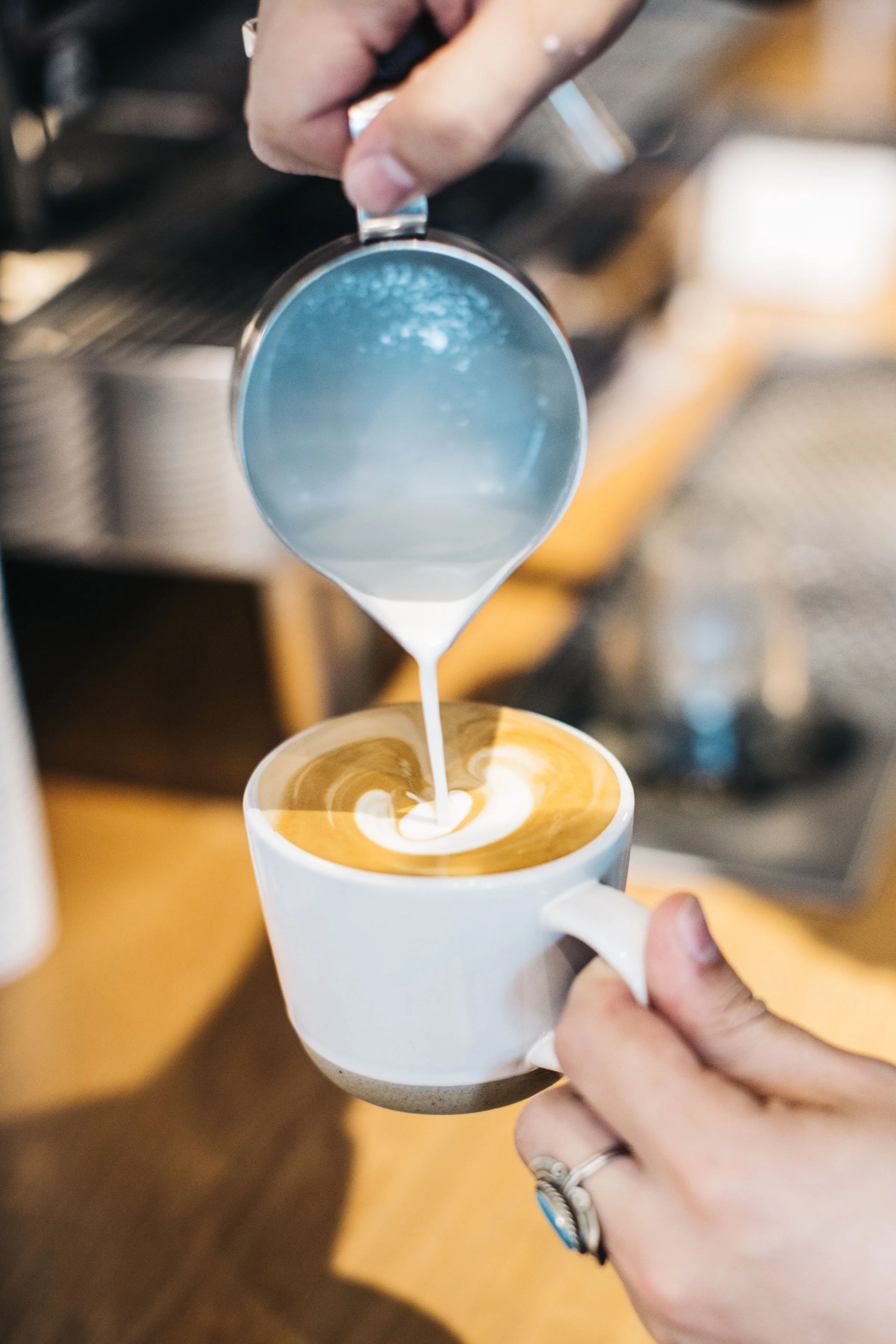 Barista pouring steamed milk into a cup of espresso to make latte art in a coffee shop.
