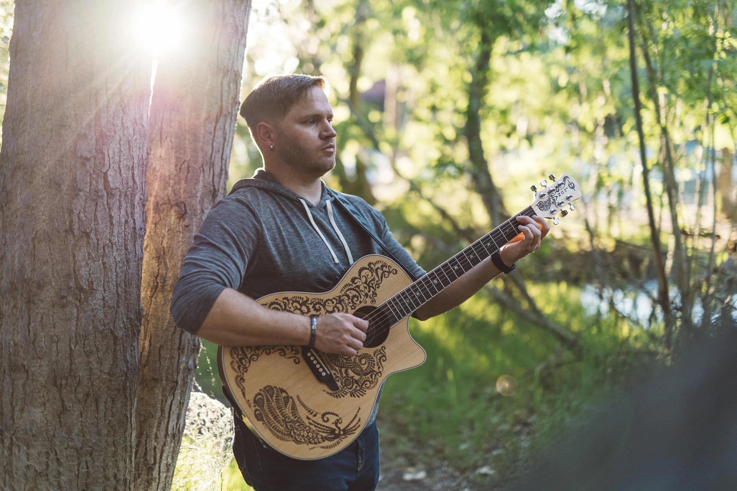 Male musician playing guitar in the trees during a branding photography session on the Boise River Greenbelt at sunset.