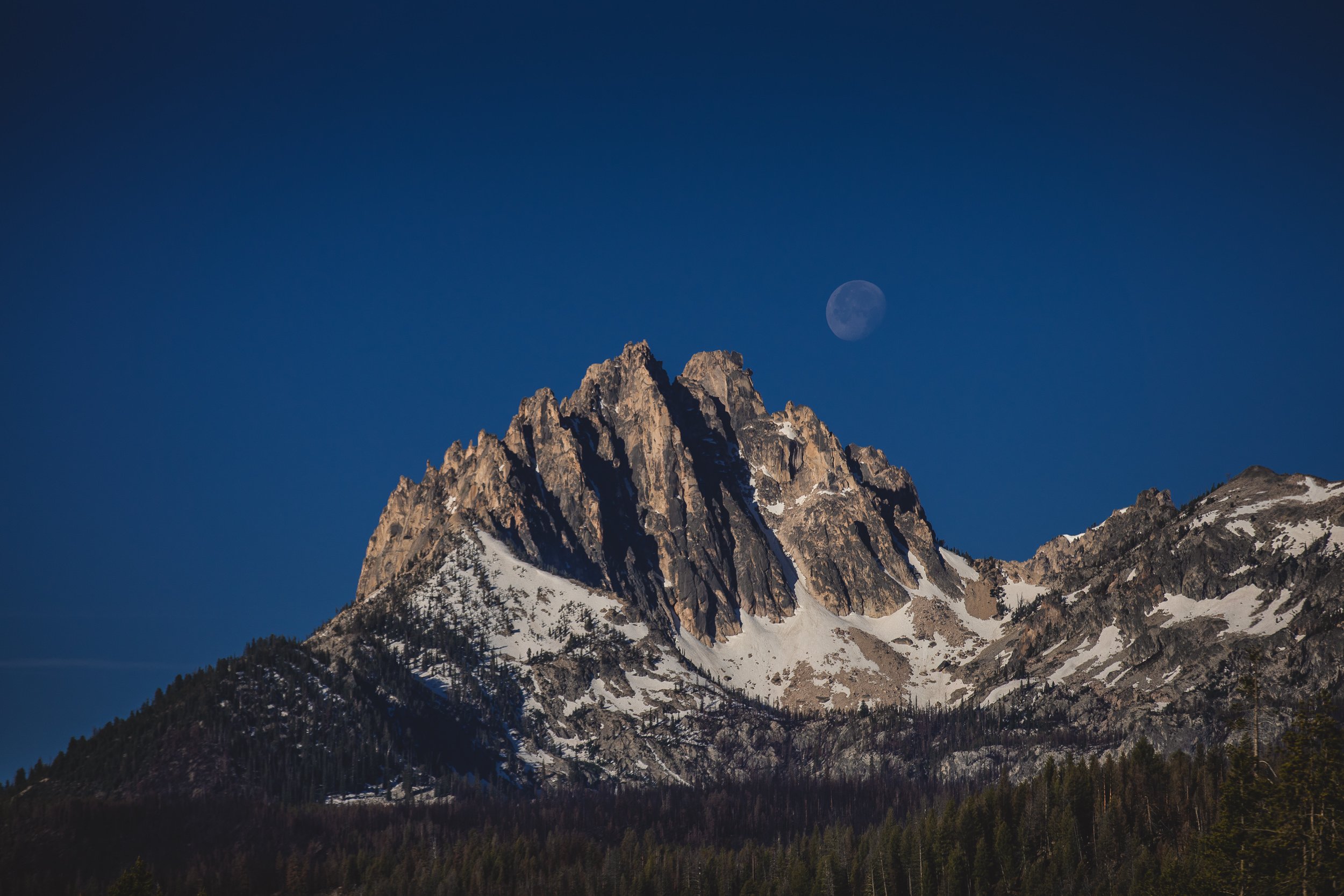 The Sawtooth Mountains with the moon above them, taken during a branding photoshoot focused on tourism in Stanley Idaho.