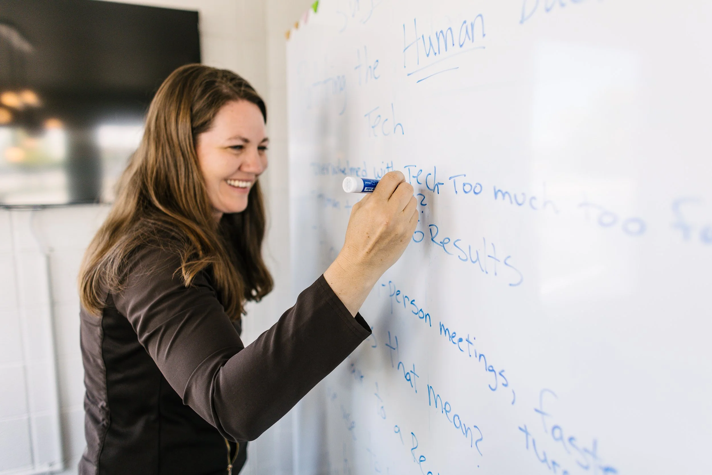 Woman entrepreneur smiling candidly while writing on a white board during a branding photoshoot in Boise, Idaho.
