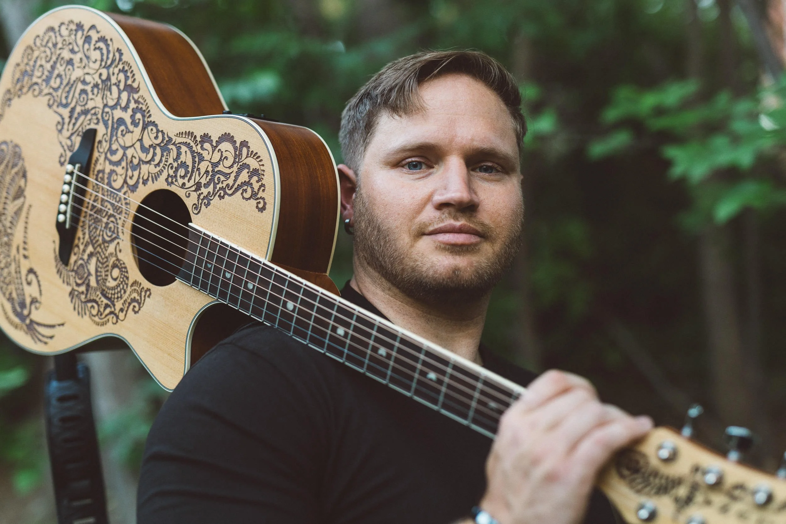 Man holding guitar over his shoulder while looking directly at camera during a personal branding photoshoot at sunset on the Boise River Greenbelt.