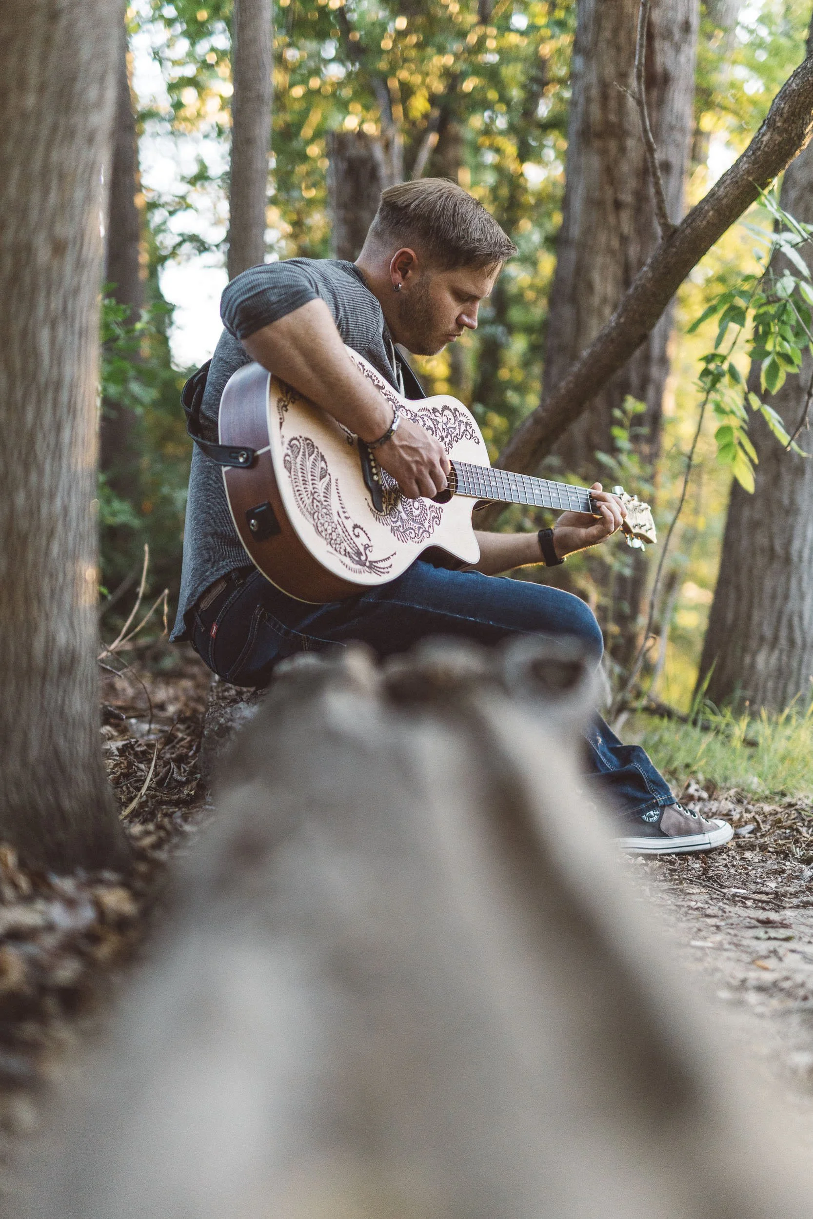 Man sitting on log playing guitar during a branding photoshoot on the Boise River Greenbelt.
