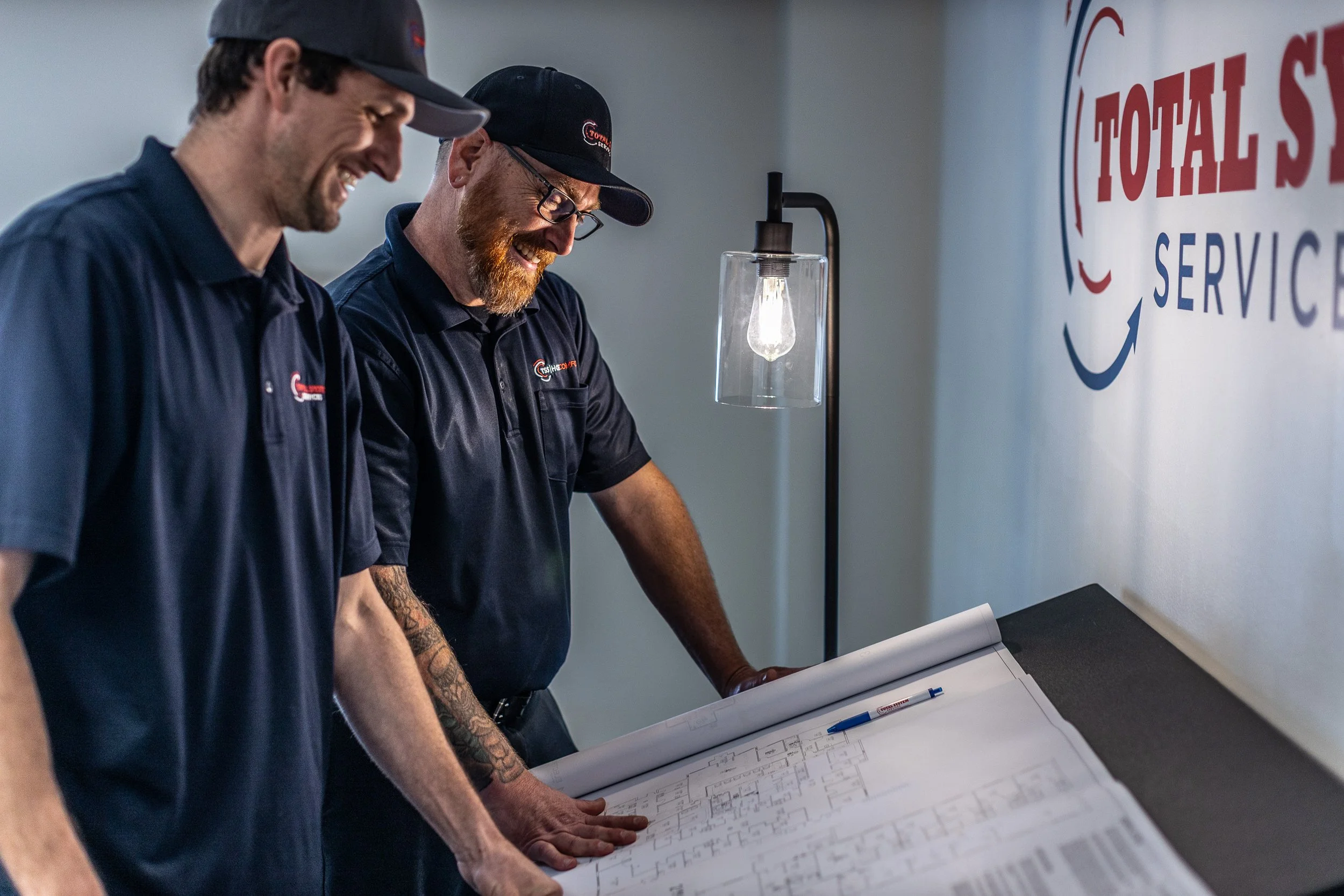 Two HVAC technicians looking at blueprints and smiling during a commercial photoshoot in Boise.