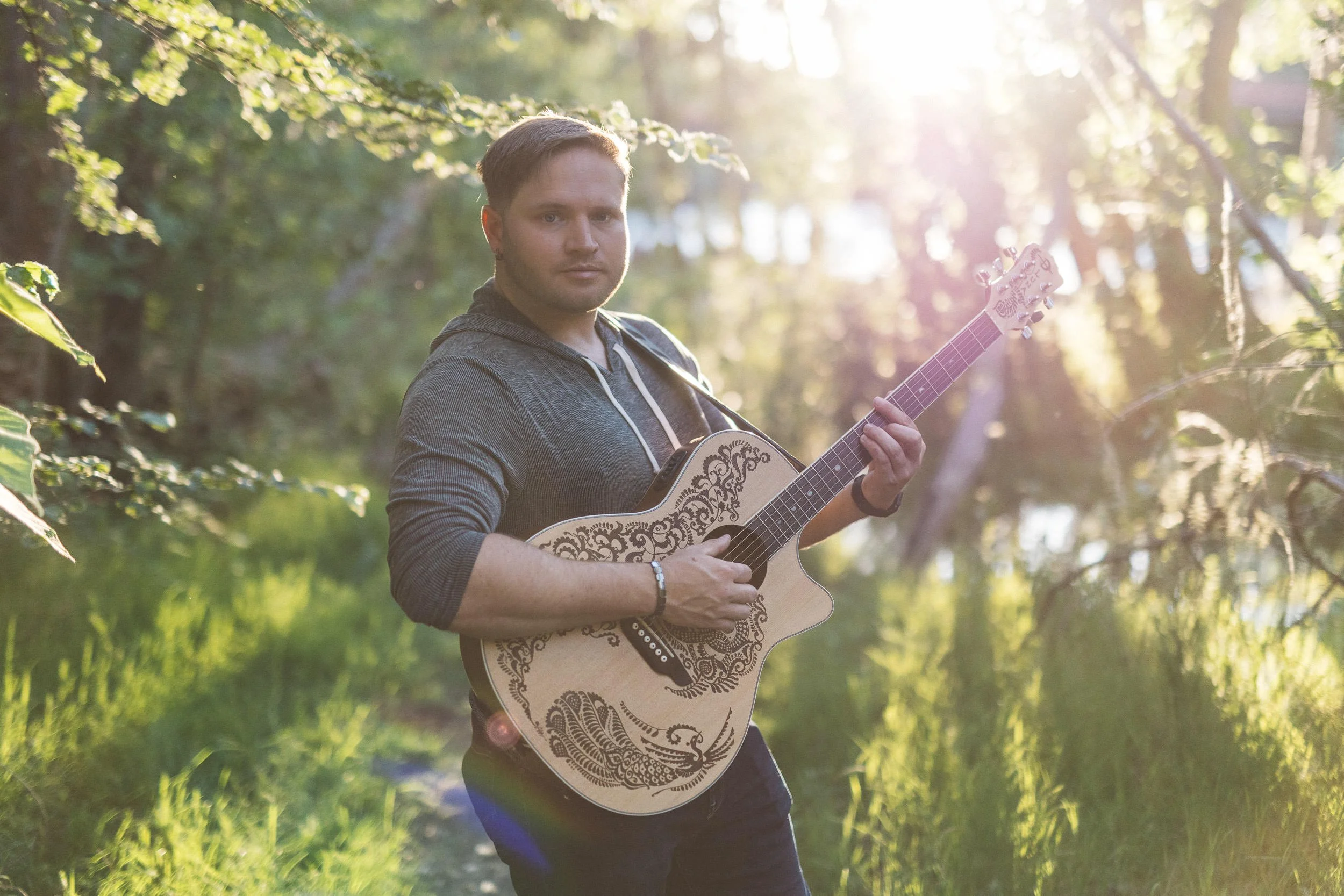 Man playing guitar with the sun behind him during a branding photoshoot at sunset on the Boise River Greenbelt.