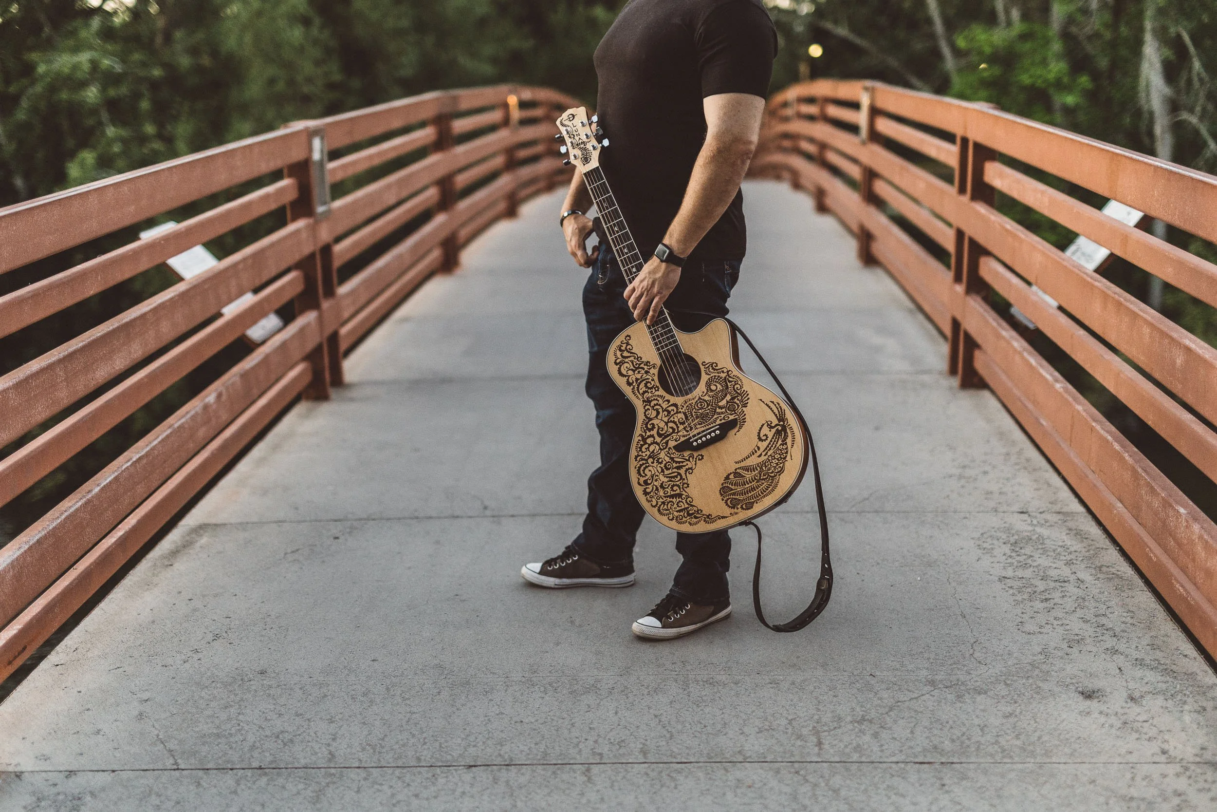 Man holding guitar on friendship bridge in Julia Davis Park, during branding photoshoot at sunset.
