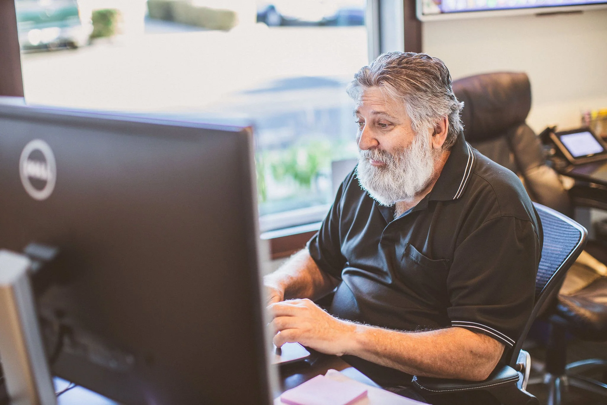 An older man with gray hair and a beard working at a desk with a computer in an office during a branding photoshoot in Newberg, Oregon.