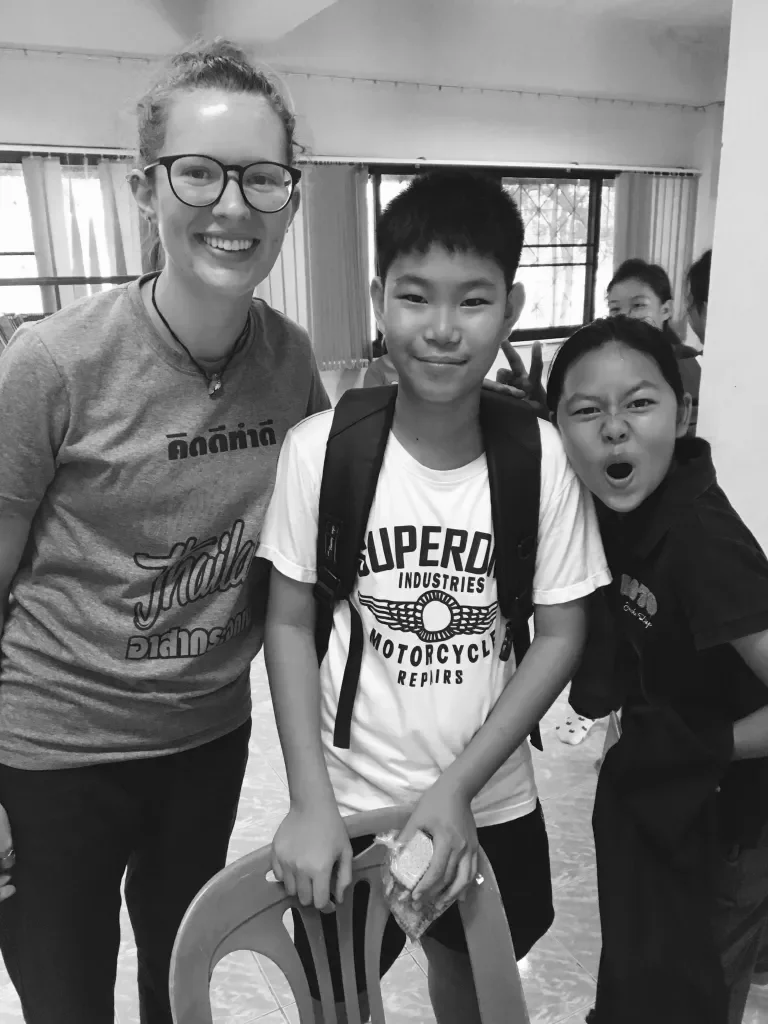 A smiling woman with glasses and three children, two girls and one boy, posing indoors with windows and curtains in the background.