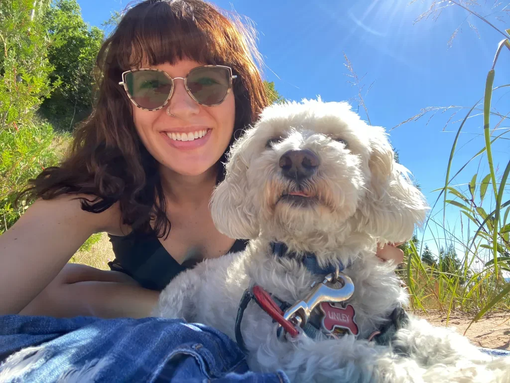 A woman with sunglasses and a dog lying on the grass outdoors on a sunny day.