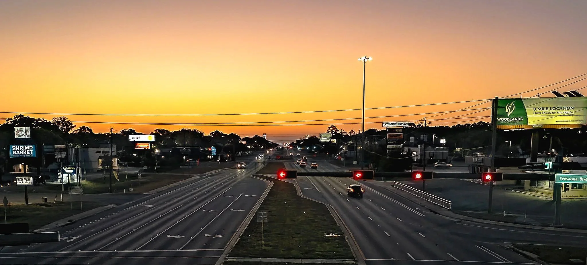 A morning roadway scene overlooking traffic, lights, and the warm glow of sunrise in the 9 Mile Pensacola area. This image combines movement, transportation, and early daylight atmosphere, making it a strong visual for regional travel, commuter stori