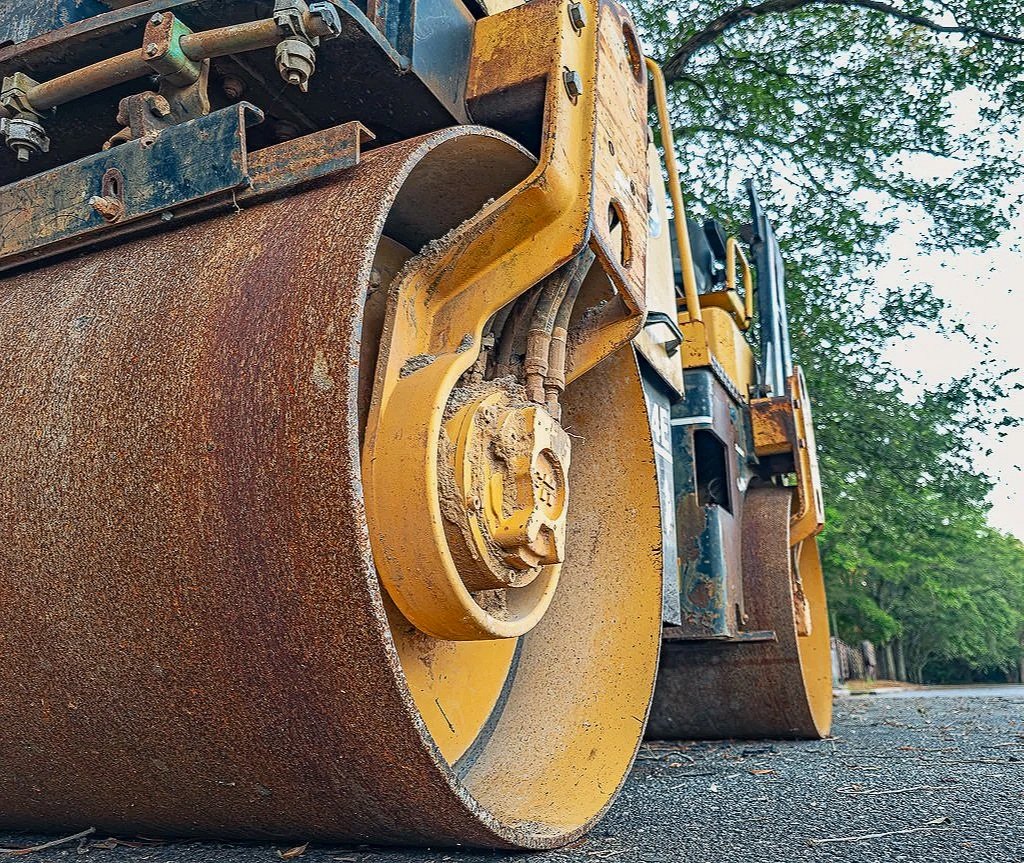 A close-up photograph of yellow construction asphalt roller with rust, metal texture, and heavy machinery detail. The image has a rugged industrial character and would work well for construction-themed prints, contractor websites, engineering portfol