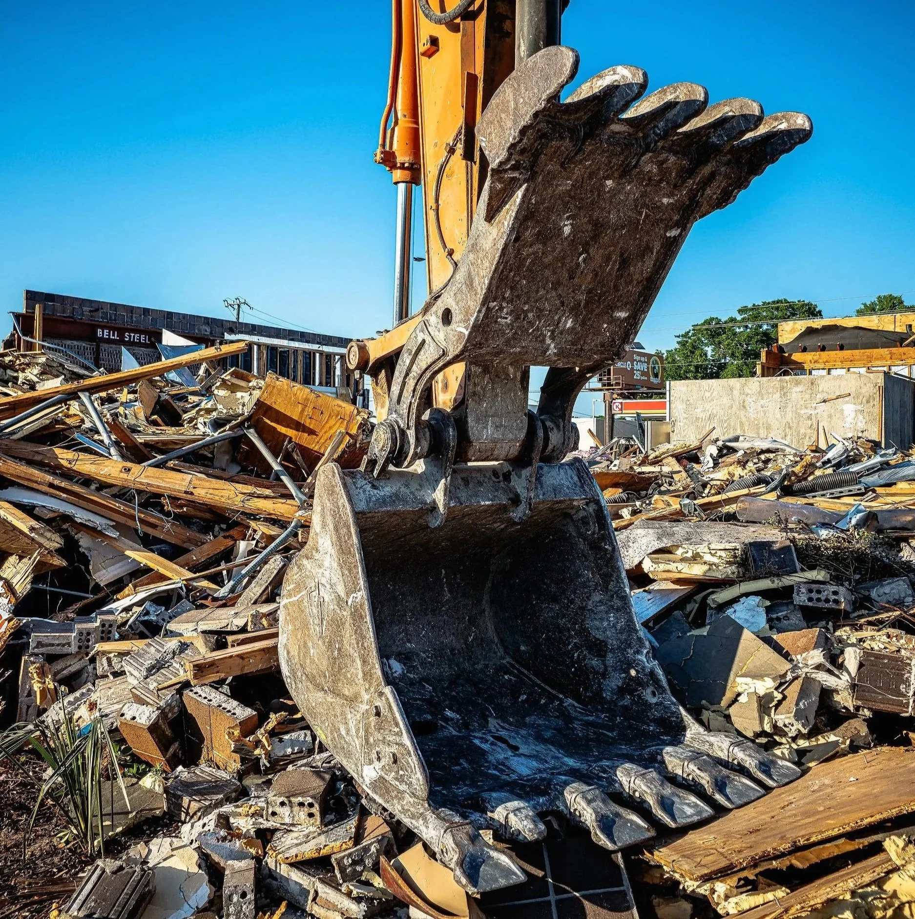 An excavator claw hangs above broken debris at a demolition site on Bayou Boulevard in Pensacola, Florida. This construction and urban infrastructure photograph captures heavy equipment, rubble, and the stark geometry of a roadside teardown in Pensac