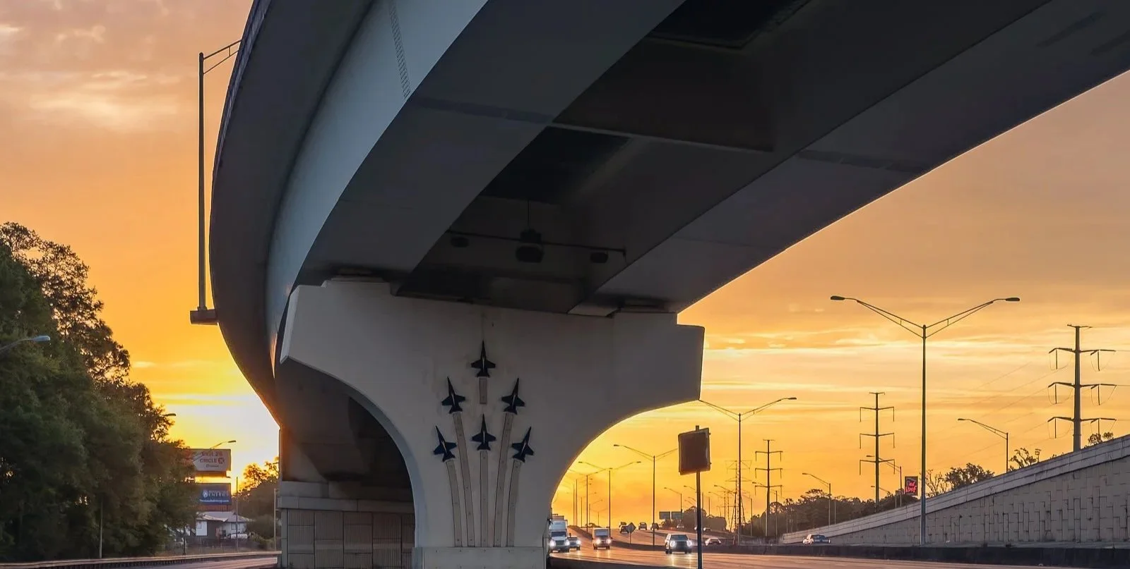 A dramatic sunrise photograph beneath the Davis Highway bridge, combining shadow, warm morning light, and strong architectural lines. This image captures the beauty of Gulf Coast infrastructure from a unique engineering-focused perspective. It works 