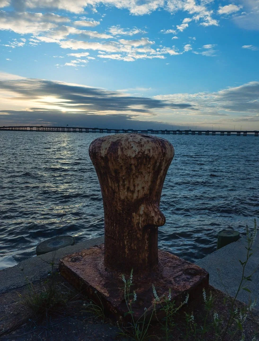A quiet Gulf Coast waterfront image featuring a weathered dock bollard silhouetted against blue water and a soft morning sky. The photograph has a calm nautical feel while still carrying an industrial edge, making it a strong option for coastal wall 