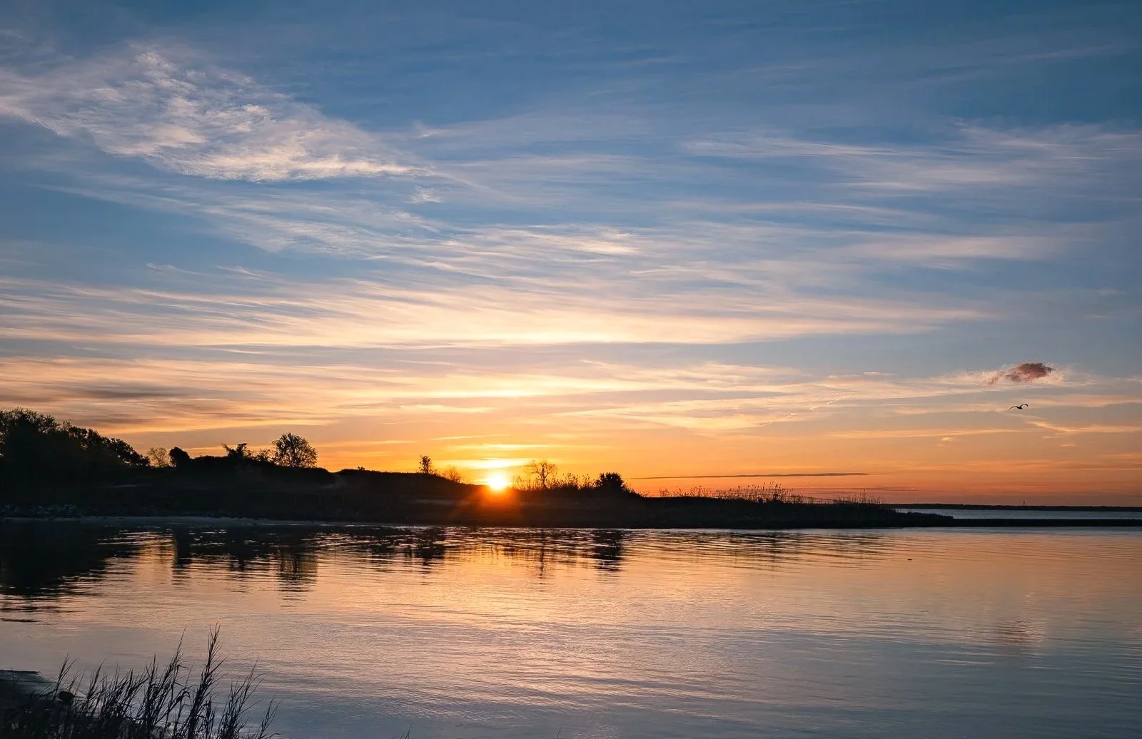 A calm Gulf Coast sunrise scene with soft orange light, blue sky, and peaceful water near the Pensacola and Gulf Breeze area. This image captures the quiet stillness of early morning on the coast, making it a strong fit for relaxing home decor, coast