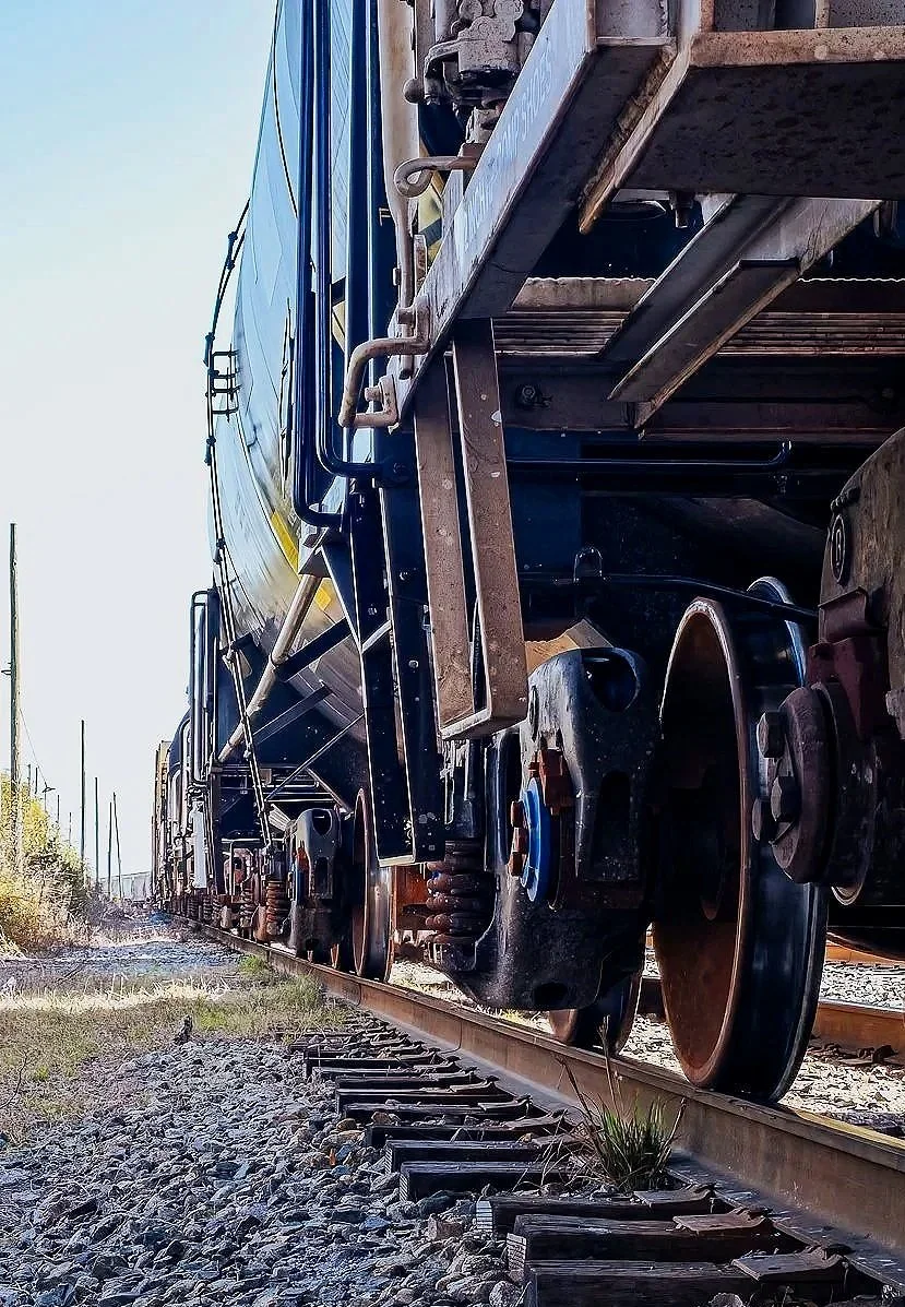 A gritty industrial photograph featuring railroad tracks, heavy machinery, metal wheels, and rugged mechanical detail. This image has a strong construction and engineering character, making it ideal for industrial wall art, transportation content, ra