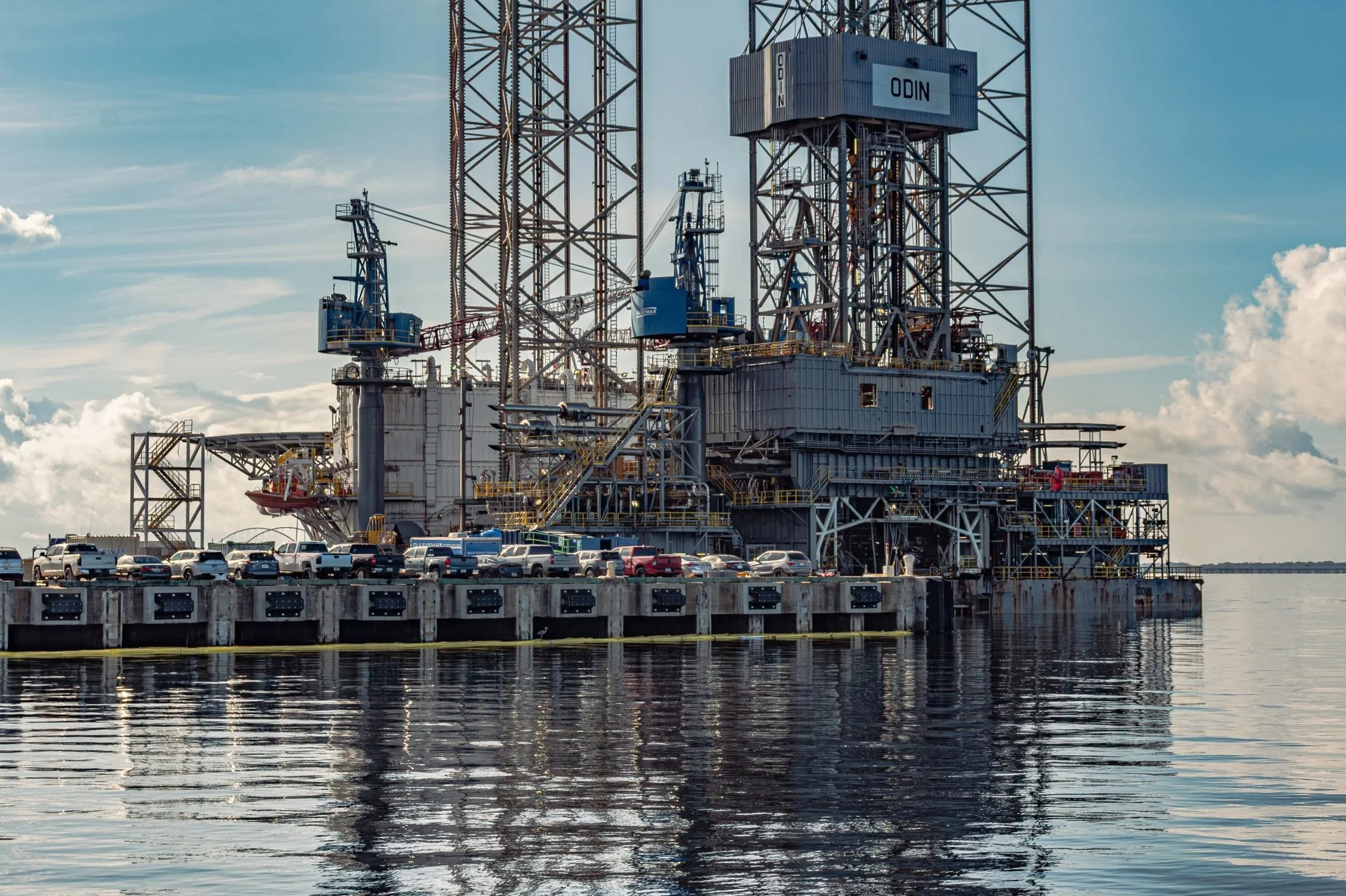 A close perspective on the crane and upper structure of the Valaris ODIN jack-up rig at the Port of Pensacola. Dock infrastructure and support vehicles frame the lower composition, reinforcing the working context of Gulf Coast offshore energy operati