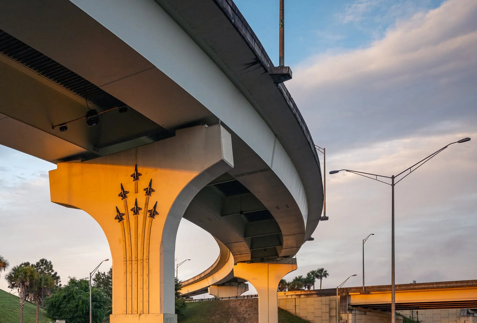 A detailed architectural image of Davis Highway Underpass with Blue Angel motifs bridge structure in Pensacola, FL, highlighting concrete columns, curved supports, and strong engineering lines. The warm light and bold composition give this photograph