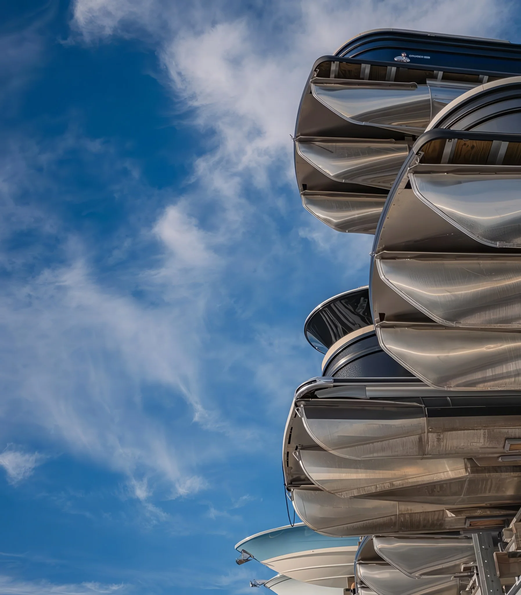 Multiple satellite dishes or antenna dishes with reflective surfaces are grouped together against a bright blue sky with scattered clouds.