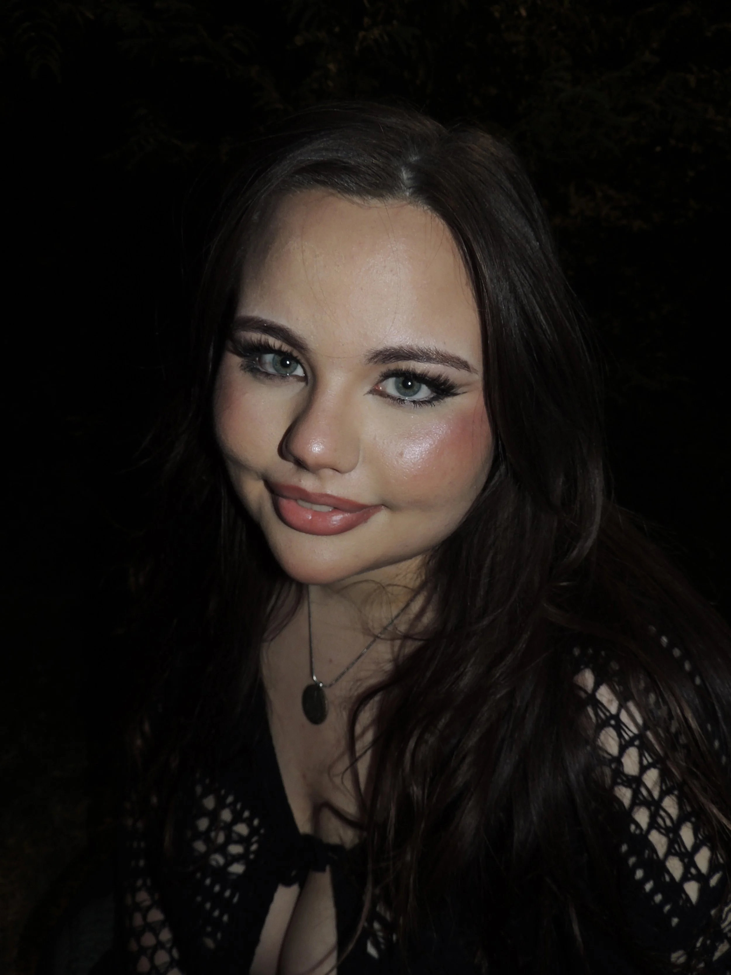 Close-up photo of a woman with blue eyes and long dark hair, smiling, with a dark background.