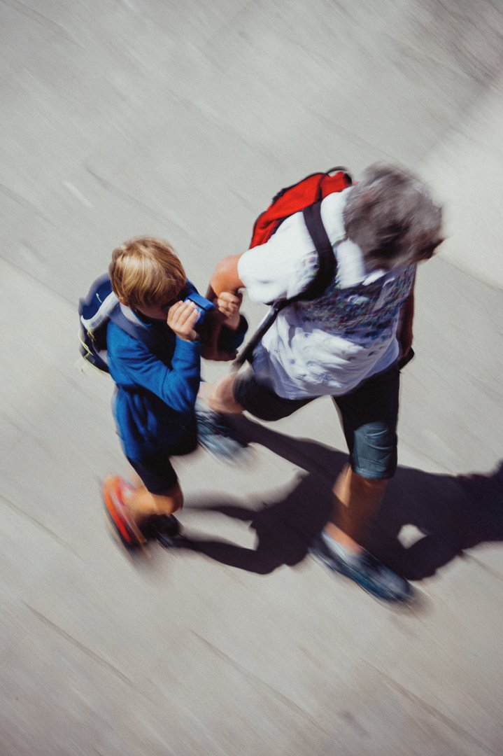 Two kids walking on a sidewalk, one appears to be helping the other.
