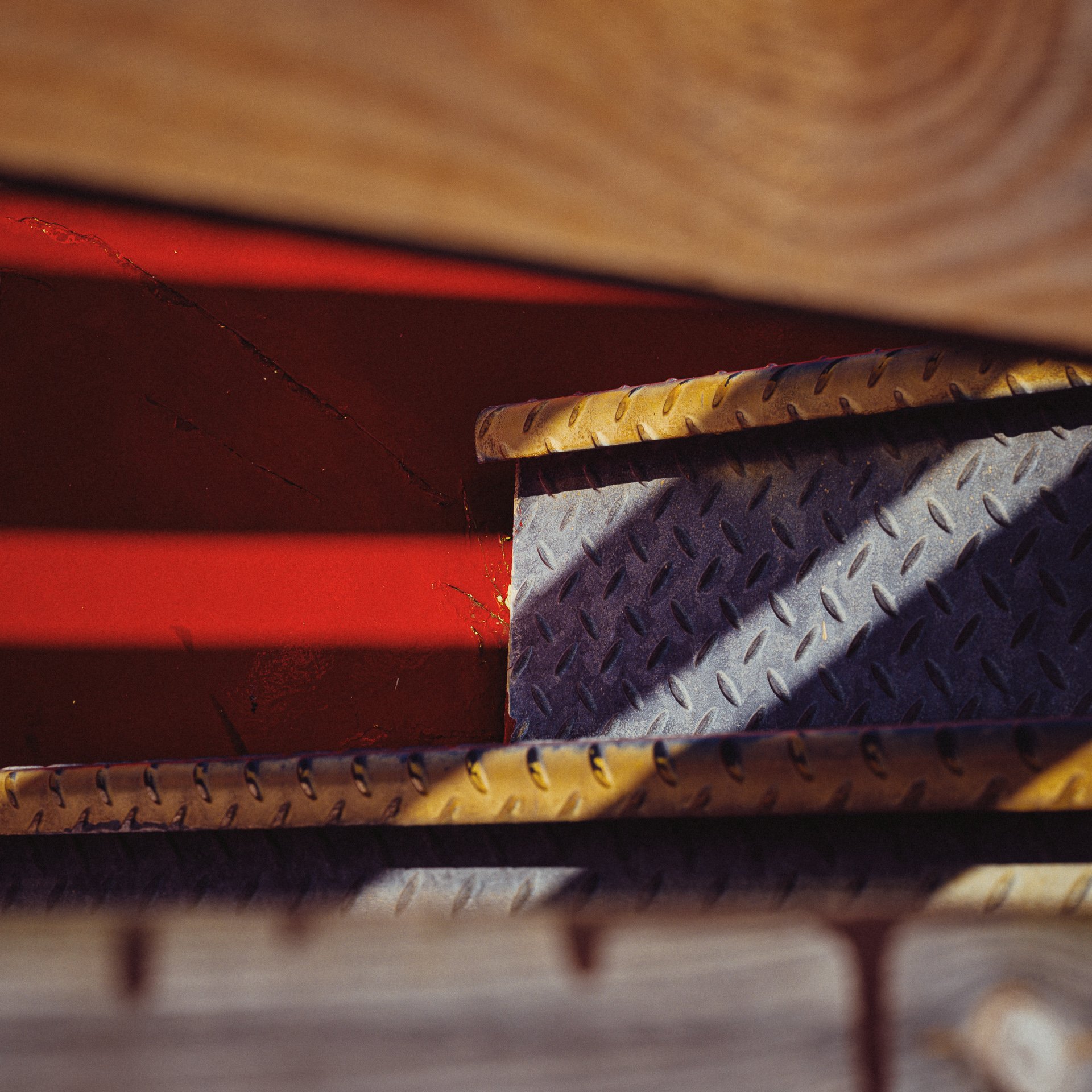 Close-up of a metal stairs with diamond plate texture, viewed from above, with red-painted sides and shadows.