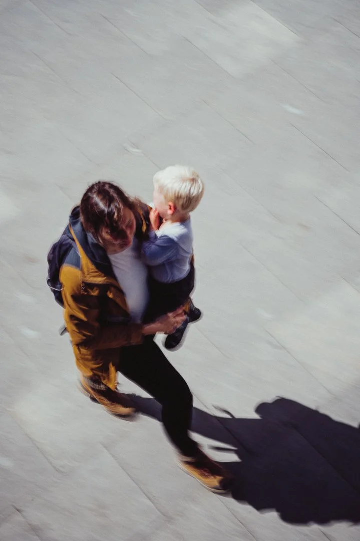 A woman holding a young boy with blonde hair, walking on a light-colored tiled floor, overhead view.