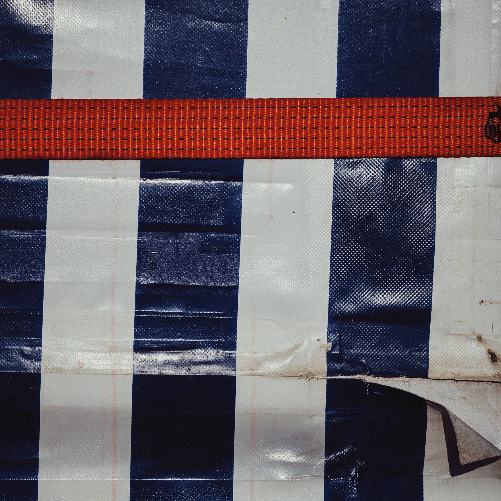 Close-up of a blue, white, and black striped tarp with a red strap running horizontally across the top.
