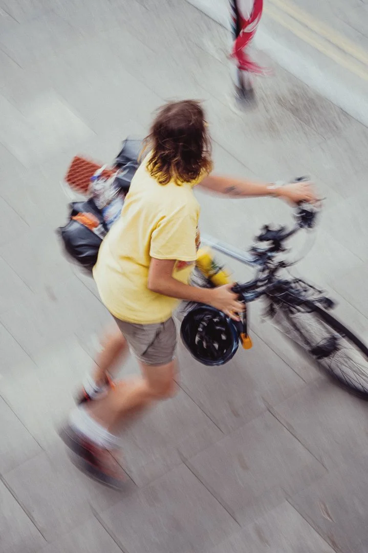 Person riding a bicycle with a backpack on a city sidewalk.