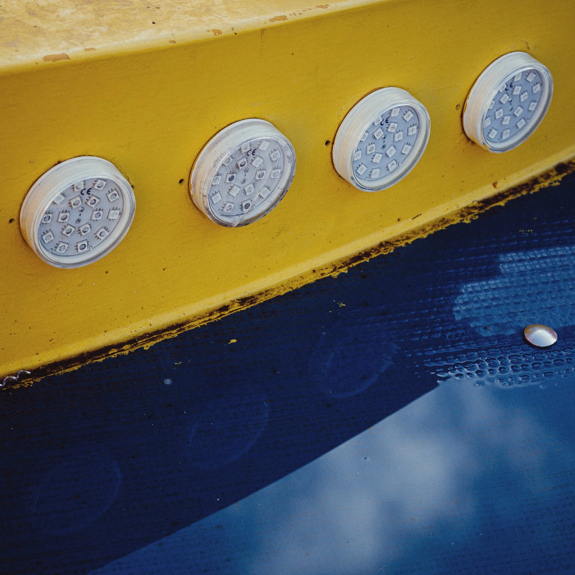 Close-up of four round LED panel lights mounted on a yellow metal surface, with a black textured surface below.