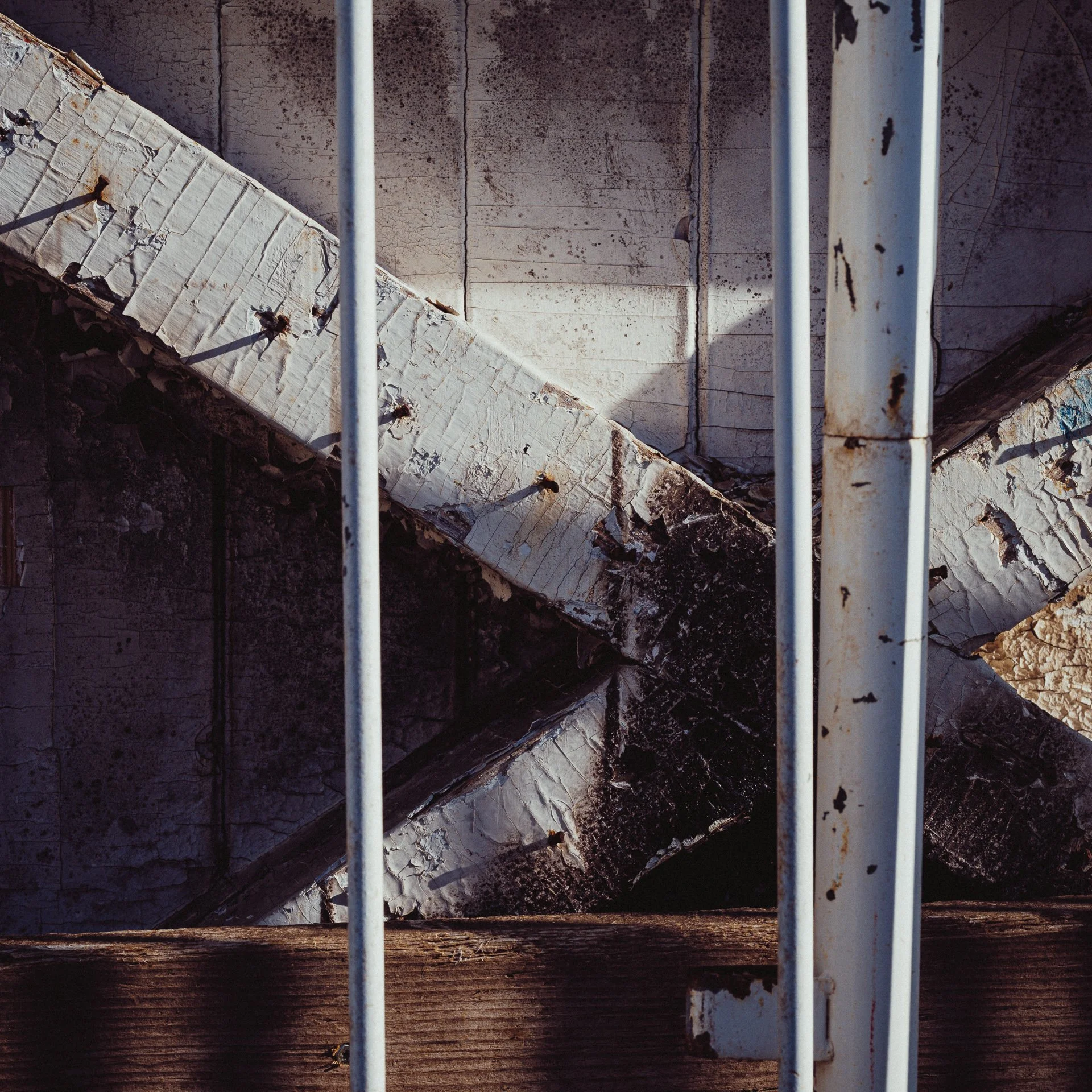 Close-up of a rusty metal fence with peeling paint, overlooking a weathered, cracked concrete rooftop.