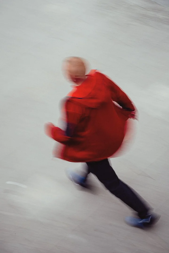 Blurry photo of a person wearing a red jacket and dark pants, running on a light-colored surface.