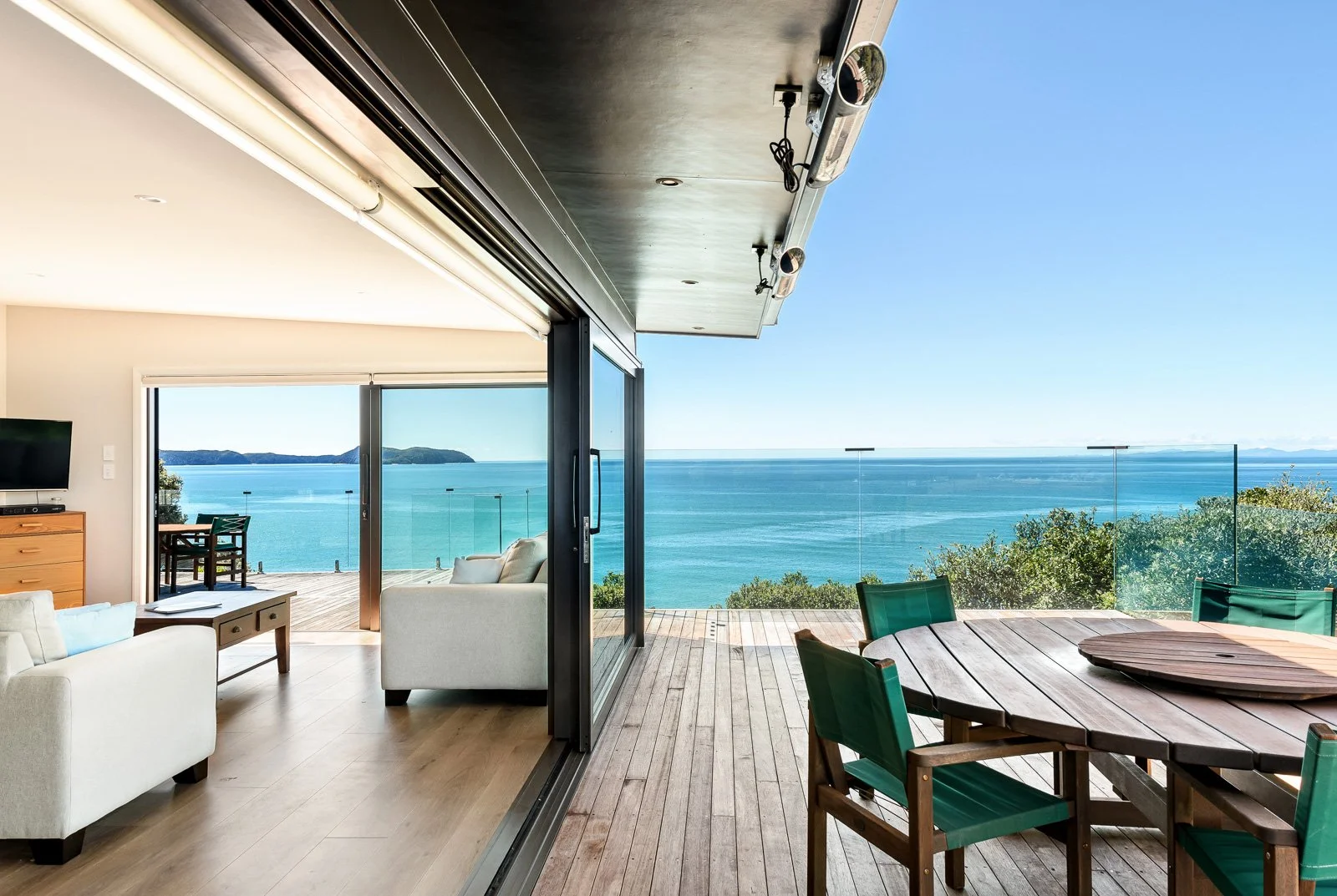 Living room with sliding glass doors opening to an outdoor deck with a panoramic ocean view, green ship, and blue sky.