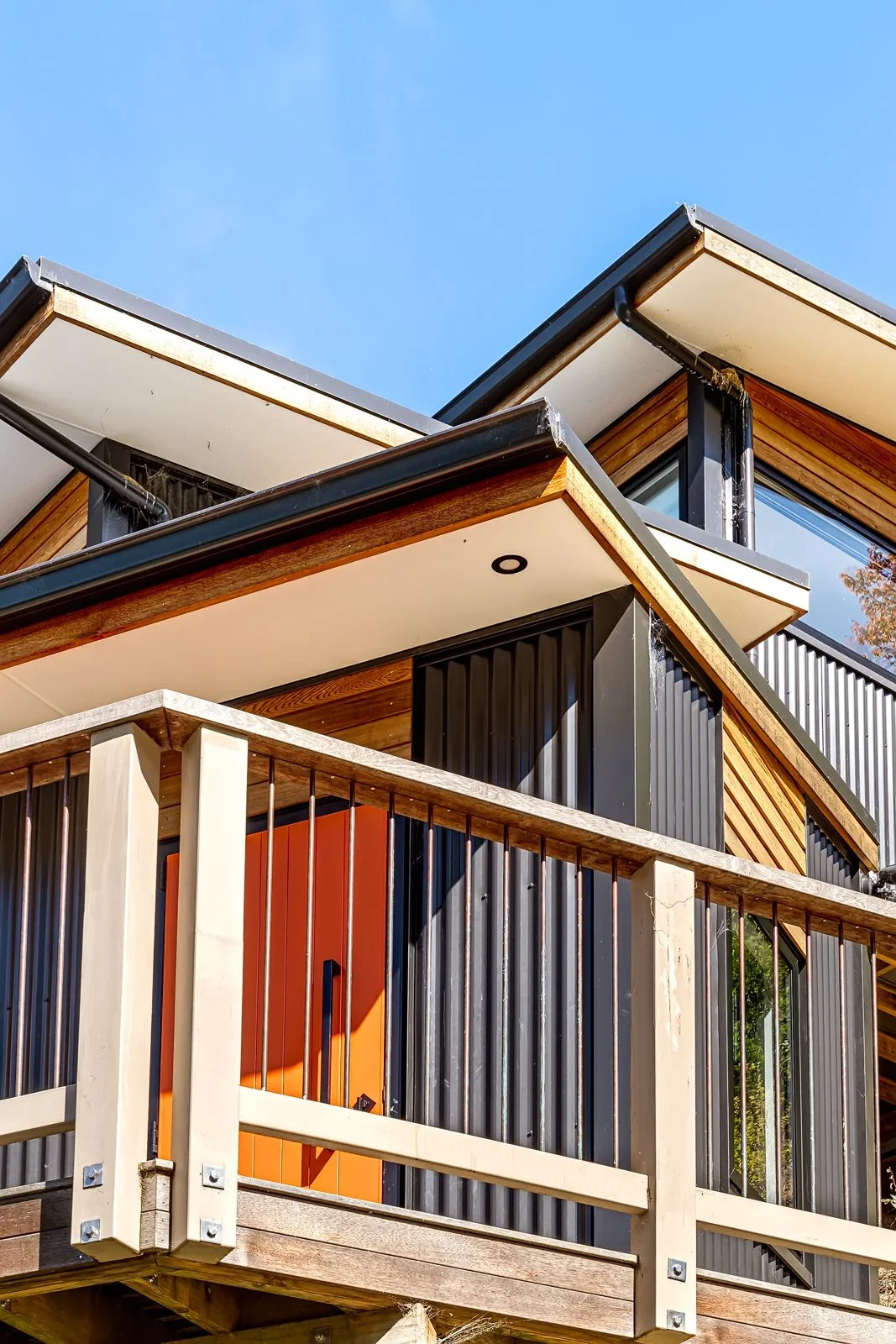 Close-up view of modern house exterior showing a balcony with railing, large windows, and a flat roof against a clear blue sky.