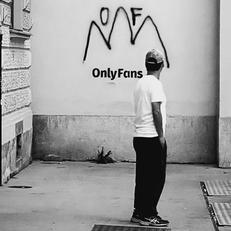 A man in a white T-shirt standing beside a wall painted with graffiti