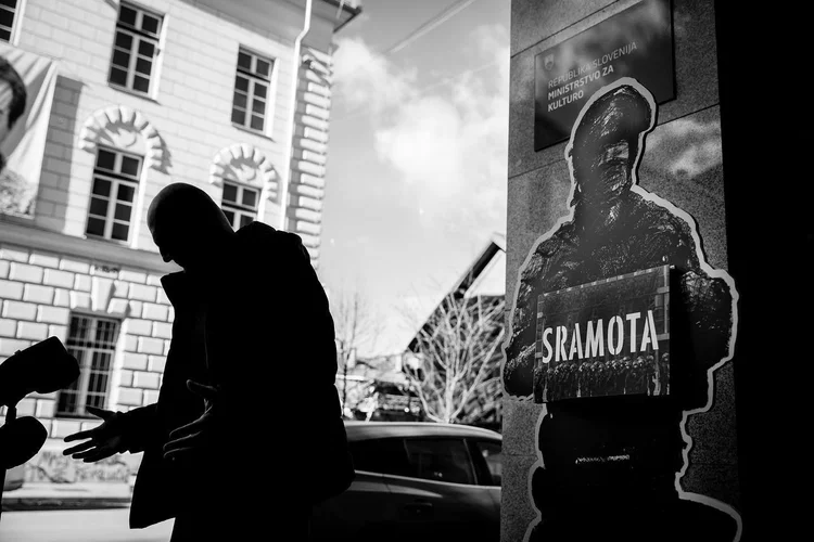 A silhouetted person passes a protest poster, photographed in black and white