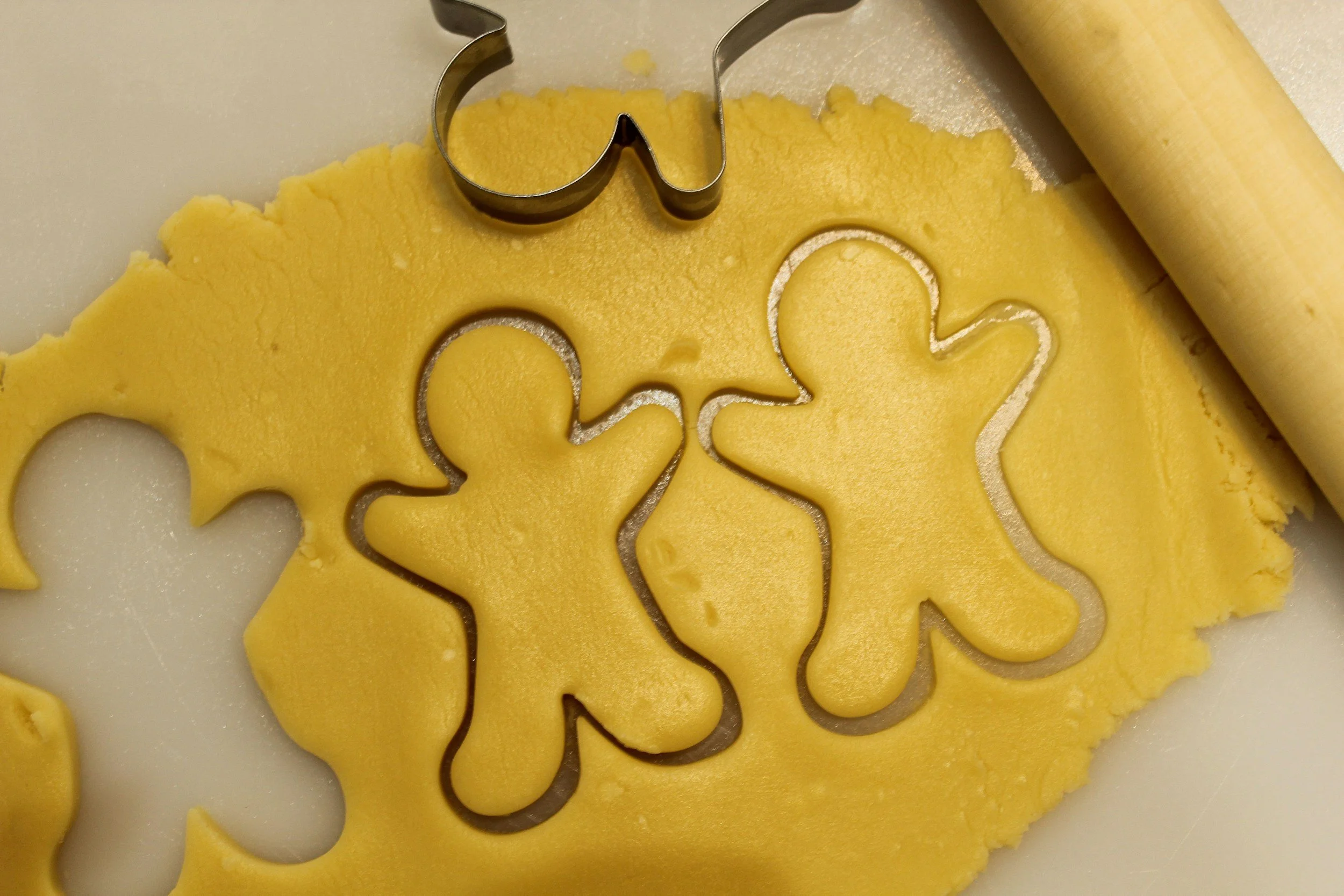 Cookie cutter in the shape of a gingerbread person pressed into rolled out cookie dough, with additional gingerbread shape cookies cut out.