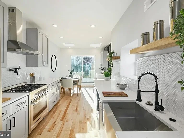 Bright, modern kitchen with white cabinetry, black faucet, wooden floating shelves, and natural light from a large window and glass door leading to an outdoor space.