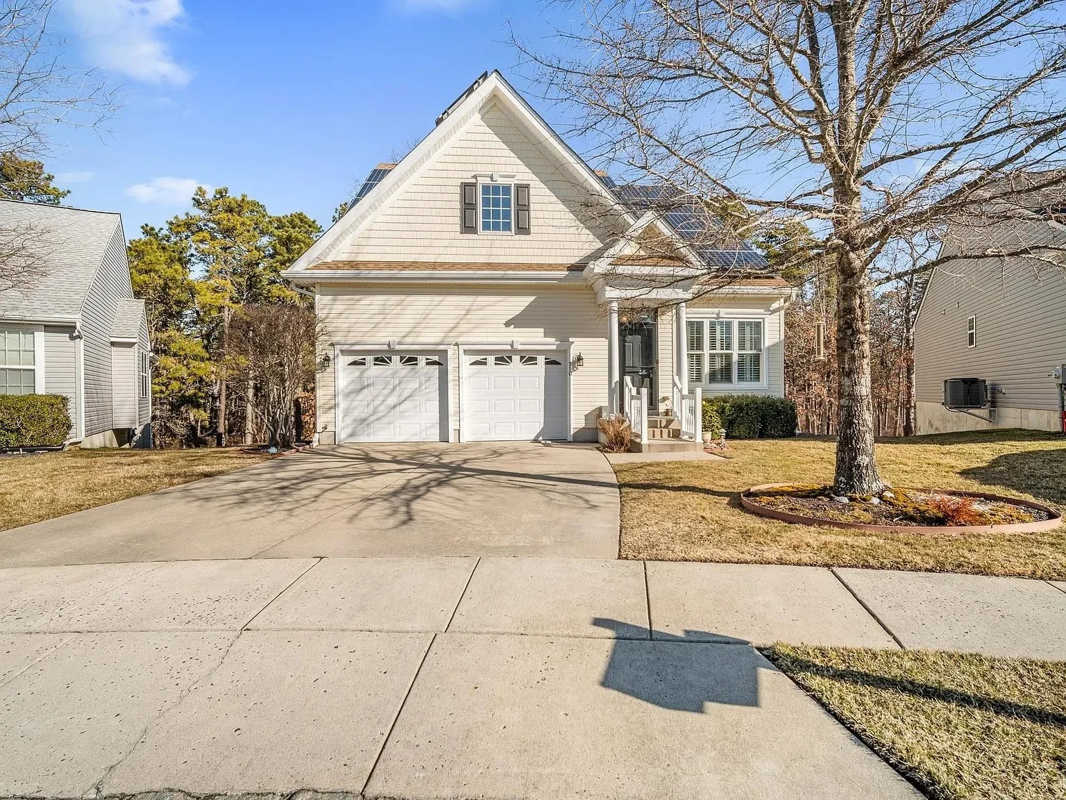 Front view of a white two-story house with a garage, a leafless tree, and a well-maintained lawn on a sunny day.