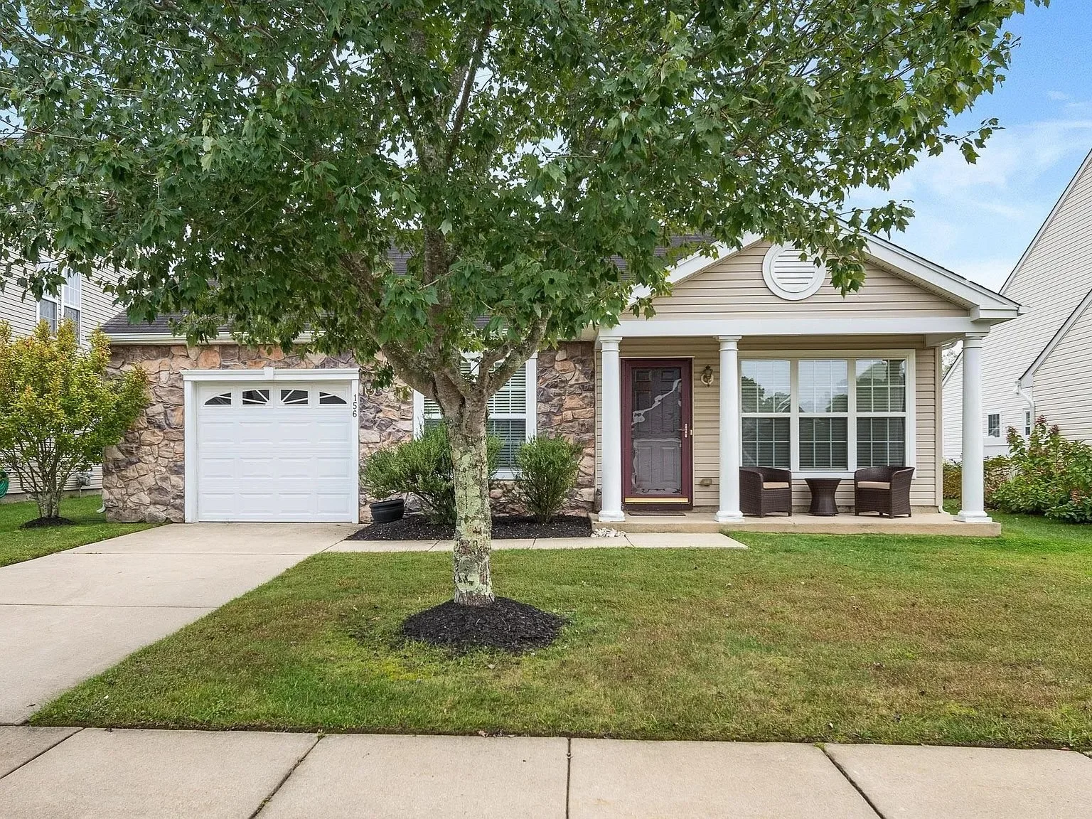 Front view of a house with a driveway, a small porch, a large tree, and lush lawn