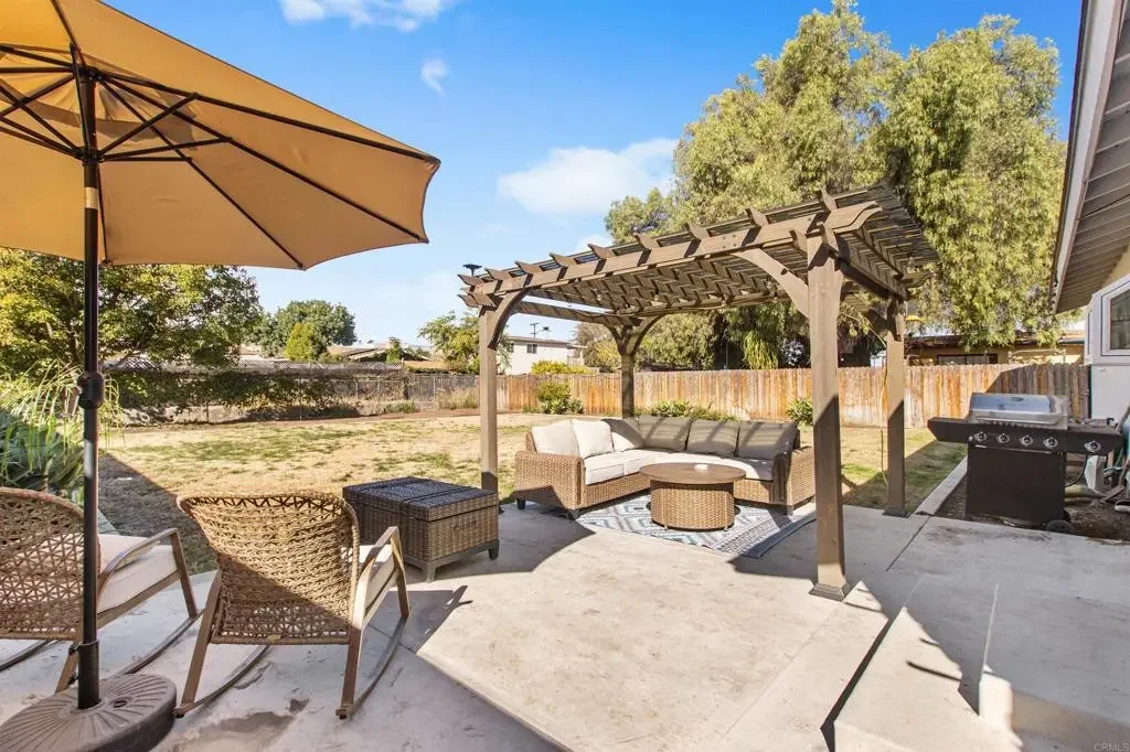 Backyard patio with outdoor seating under a pergola, an umbrella, and a barbecue grill.