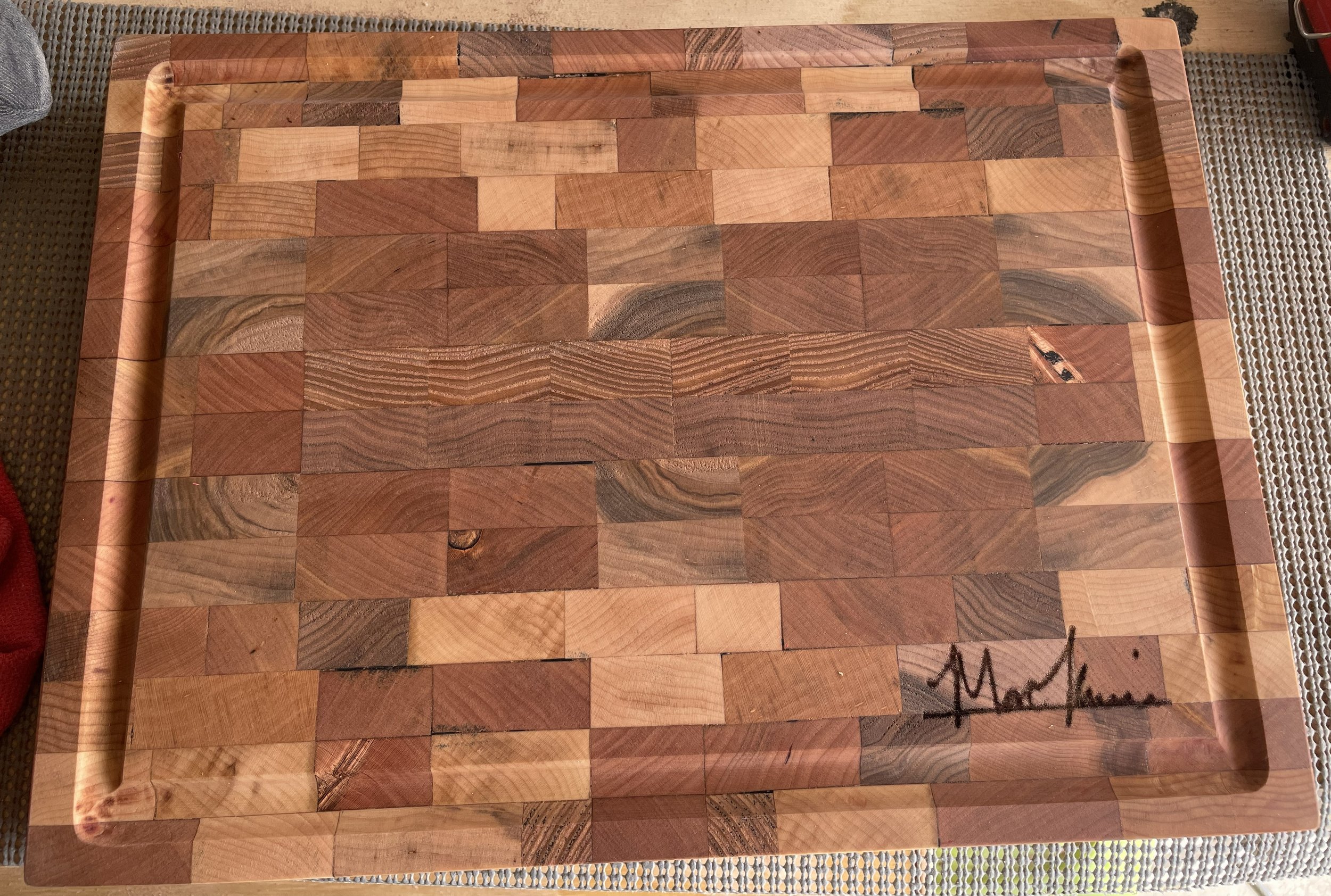 A wooden tray with a patchwork pattern of different types of wood, featuring a signature in the bottom right corner.