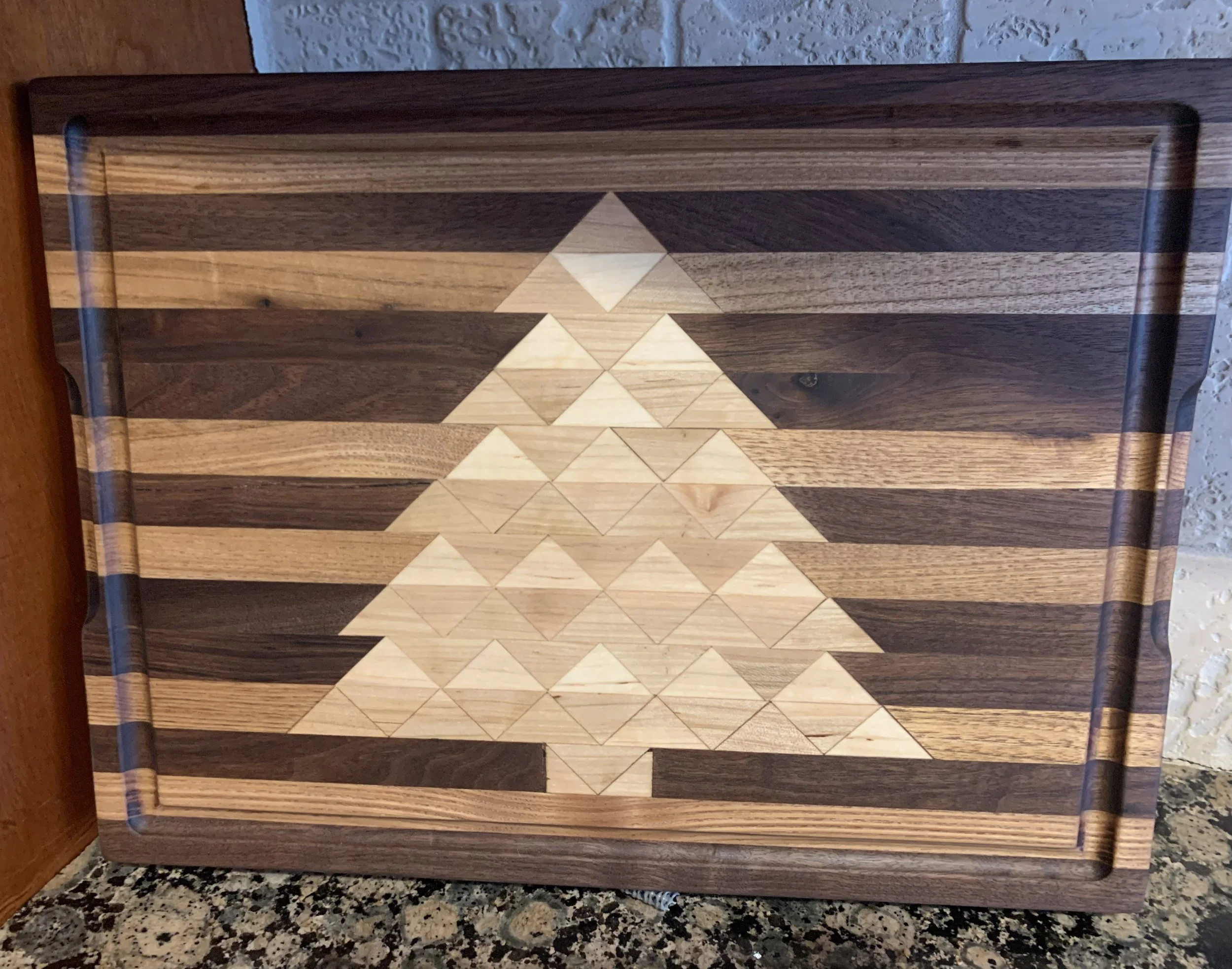 A wooden cutting board with a geometric pattern of light and dark wood in the shape of a triangle within a rectangular frame.