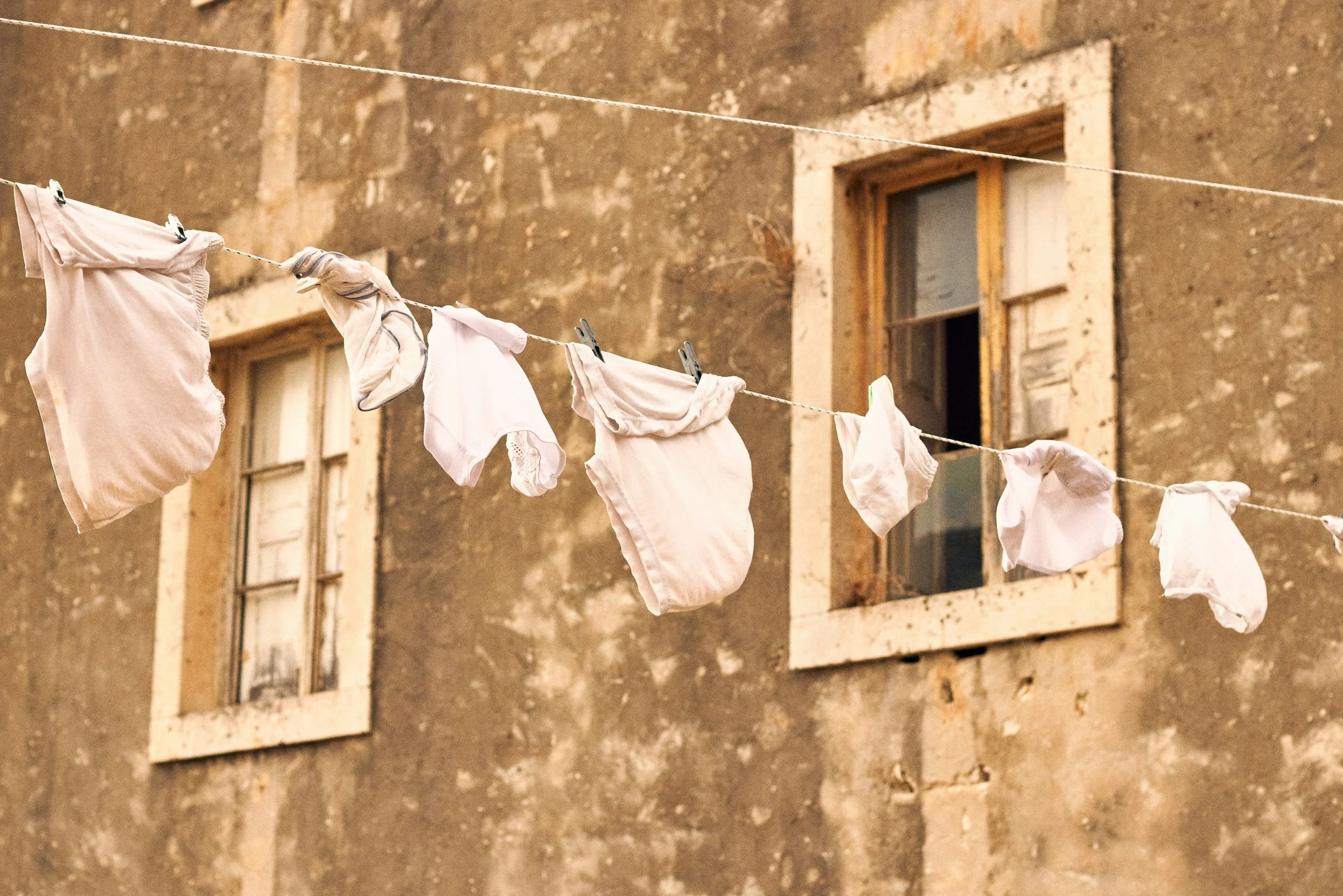 Clothes hang on a clothesline in front of an old, weathered building with open window shutters.