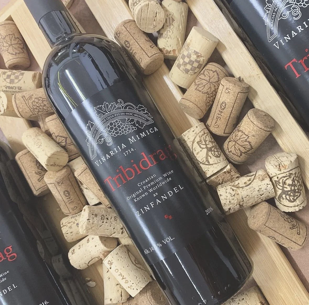 A black wine bottle labeled "Tribidrag" lying on a bed of wine corks and wooden slats. This is Zinfandel wine produced in Omis, Croatia.