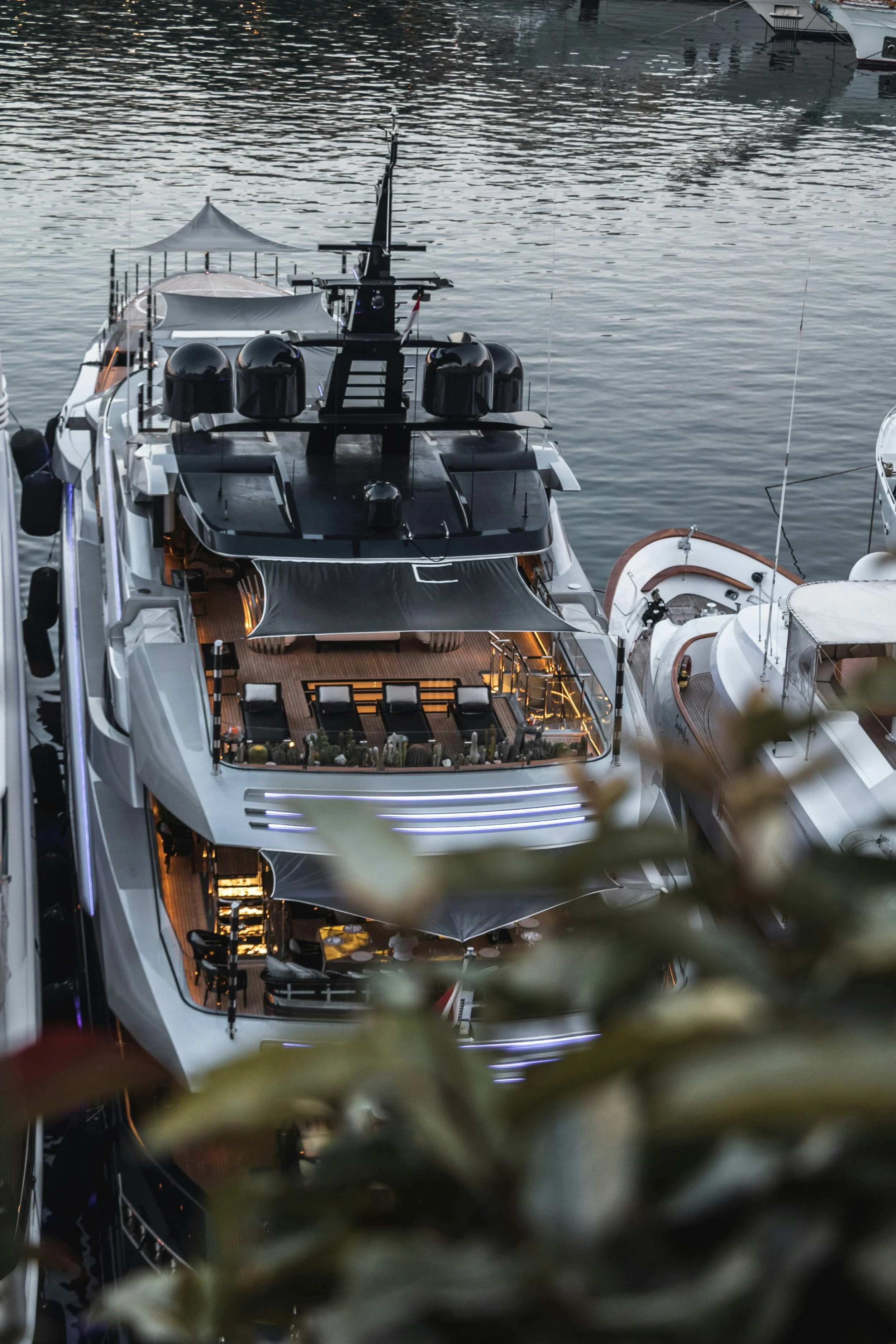 A luxurious yacht docked at a Croatian marina during evening, with multiple deck levels, shade sails, and outdoor seating areas, reflecting in the calm water.