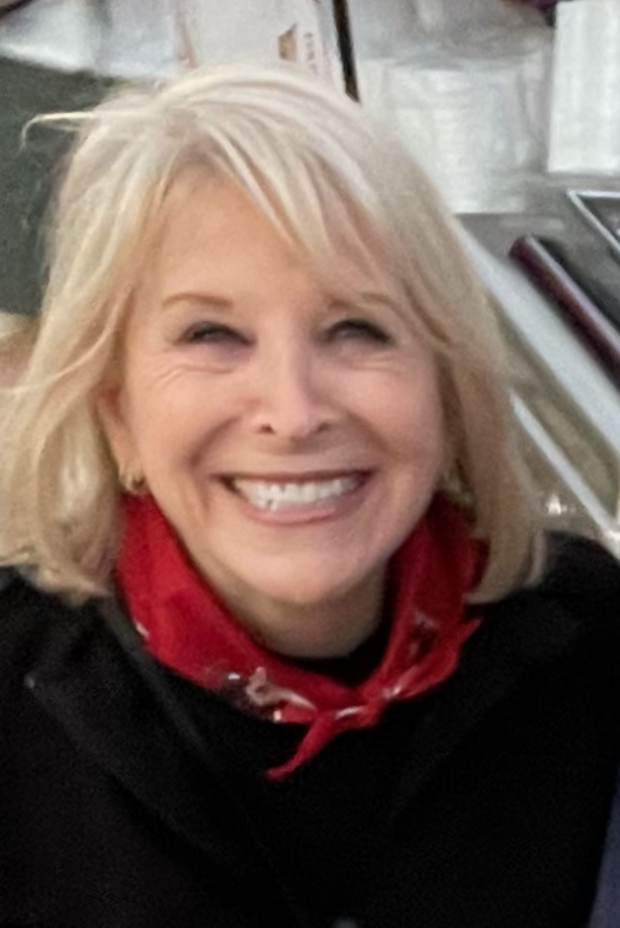 A woman with blonde hair smiling widely at the camera in a retail or grocery store setting.